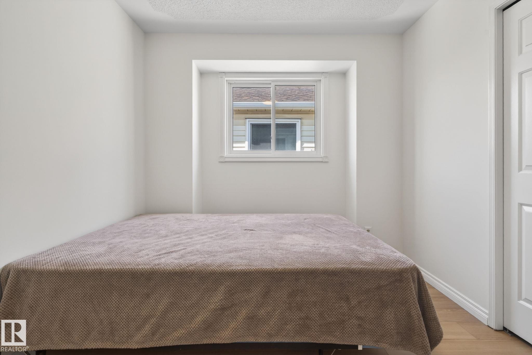 Neutral interior room featuring a recessed window, light wood-finish flooring, and a white paneled door - 8403 190 Street, Edmonton, AB - Indoor Photo Showing Bedroom