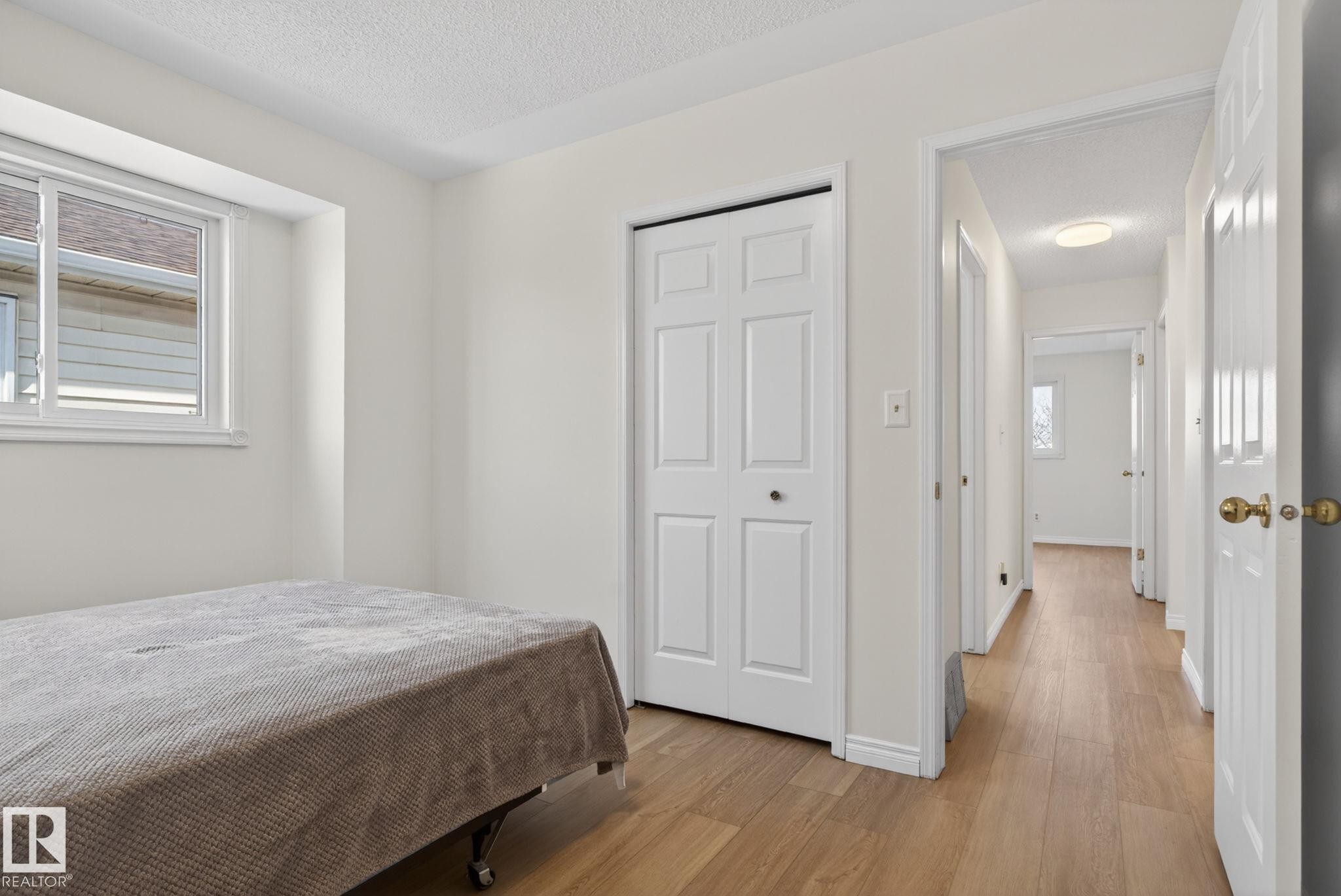 Bedroom featuring a sliding window, bi-fold closet doors, and wood-finish flooring extending into the hallway - 8403 190 Street, Edmonton, AB - Indoor Photo Showing Bedroom