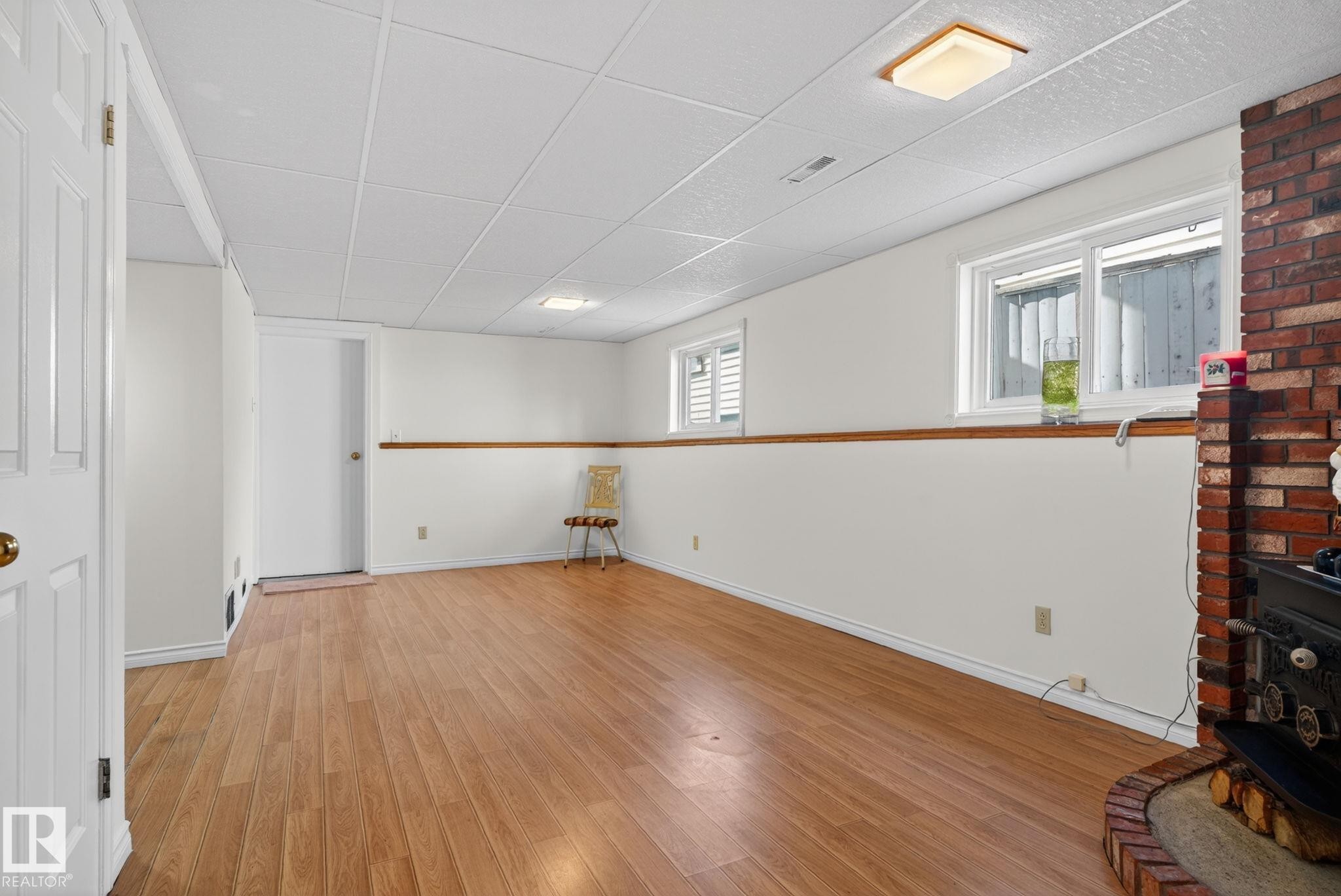 Spacious room featuring wood-finish flooring, white walls, and a drop ceiling - 8403 190 Street, Edmonton, AB - Indoor Photo Showing Other Room