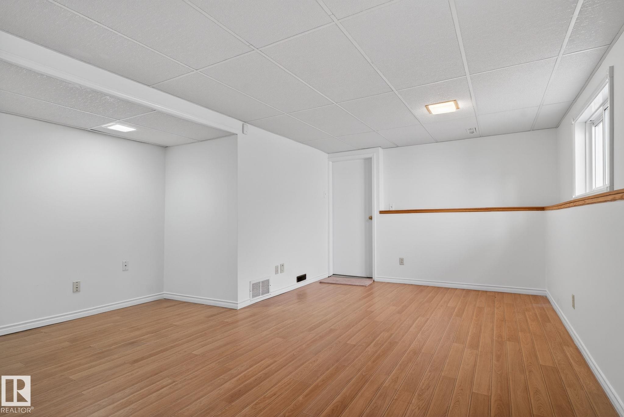 Spacious room featuring wood-finish flooring, white walls, and a drop ceiling with recessed lighting - 8403 190 Street, Edmonton, AB - Indoor Photo Showing Other Room
