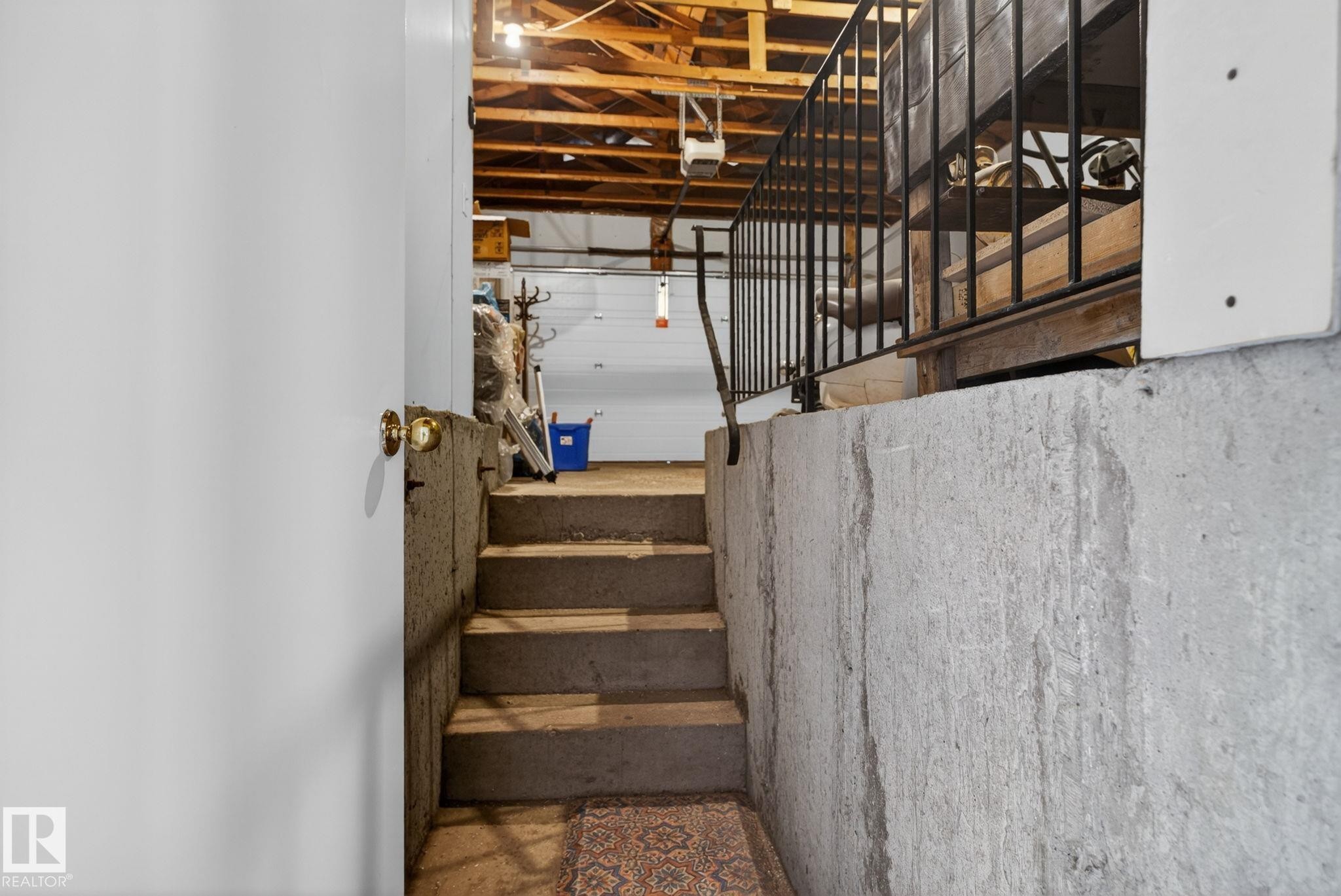 Concrete steps leading to an exposed ceiling structure with visible wooden beams, featuring a dark metal railing and a partial garage door - 8403 190 Street, Edmonton, AB - Indoor Photo Showing Other Room