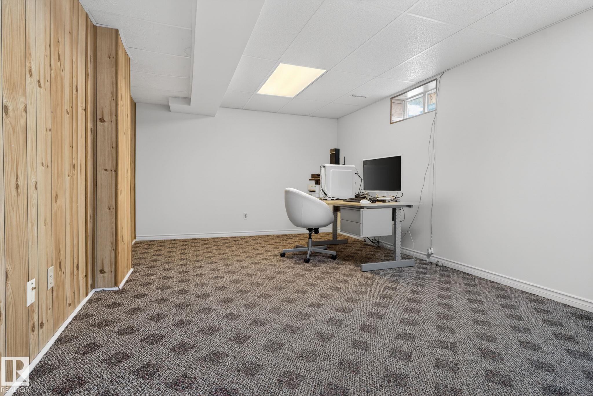 Spacious room featuring patterned carpeting, white walls, and a wood-paneled accent wall - 8403 190 Street, Edmonton, AB - Indoor