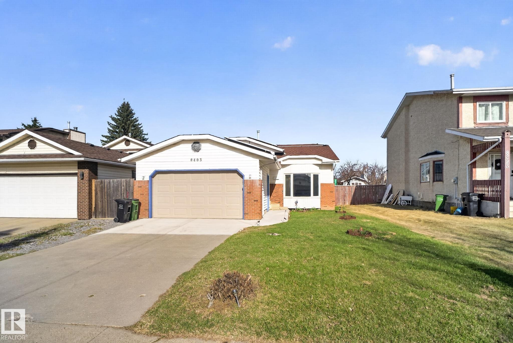 Single-story residence featuring a two-car garage with a tan door, brick facade accents, and a bay window - 8403 190 Street, Edmonton, AB - Outdoor