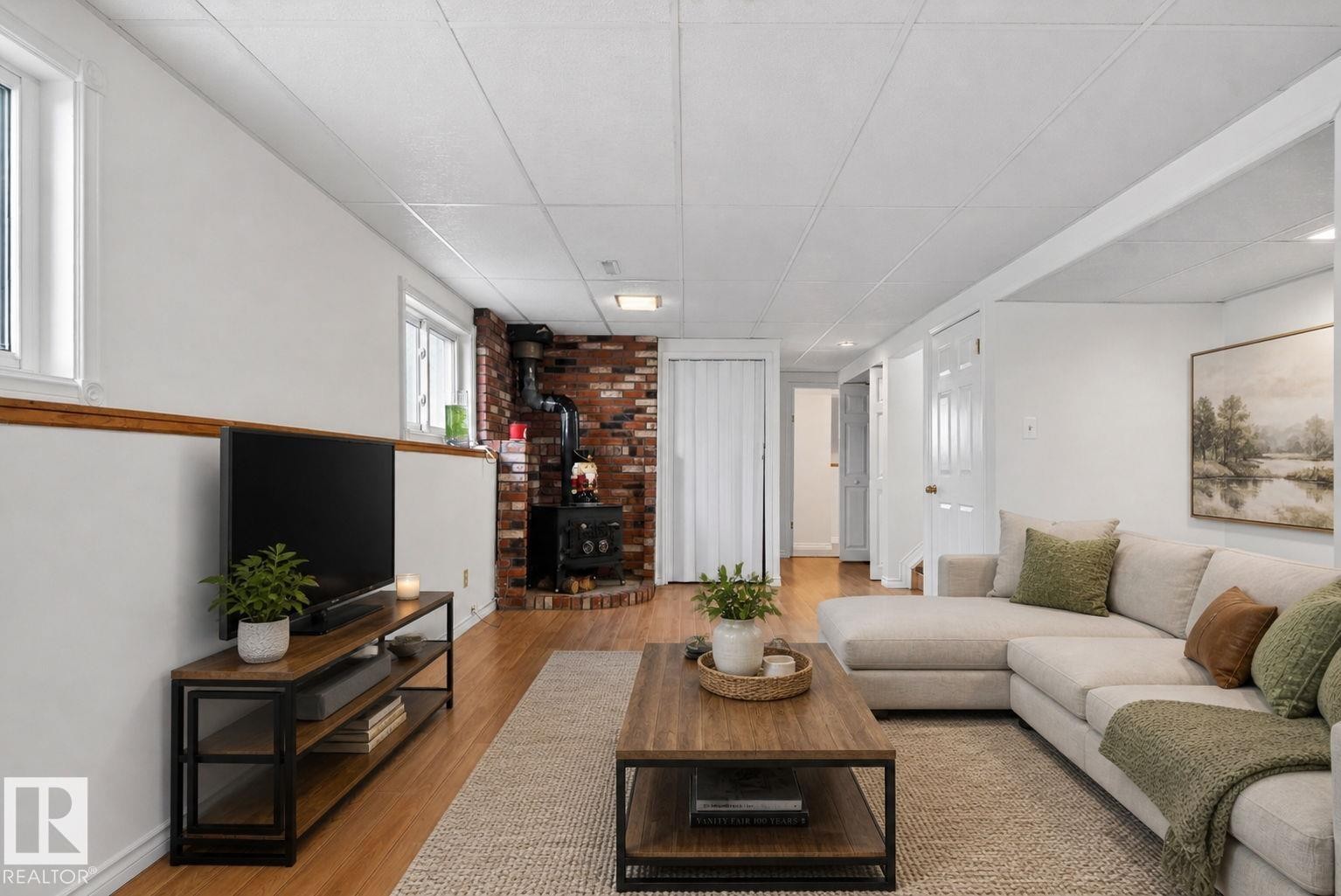 Open living space featuring wood-finish flooring, a brick accent wall, and a corner wood-burning stove - 8403 190 Street, Edmonton, AB - Indoor Photo Showing Living Room