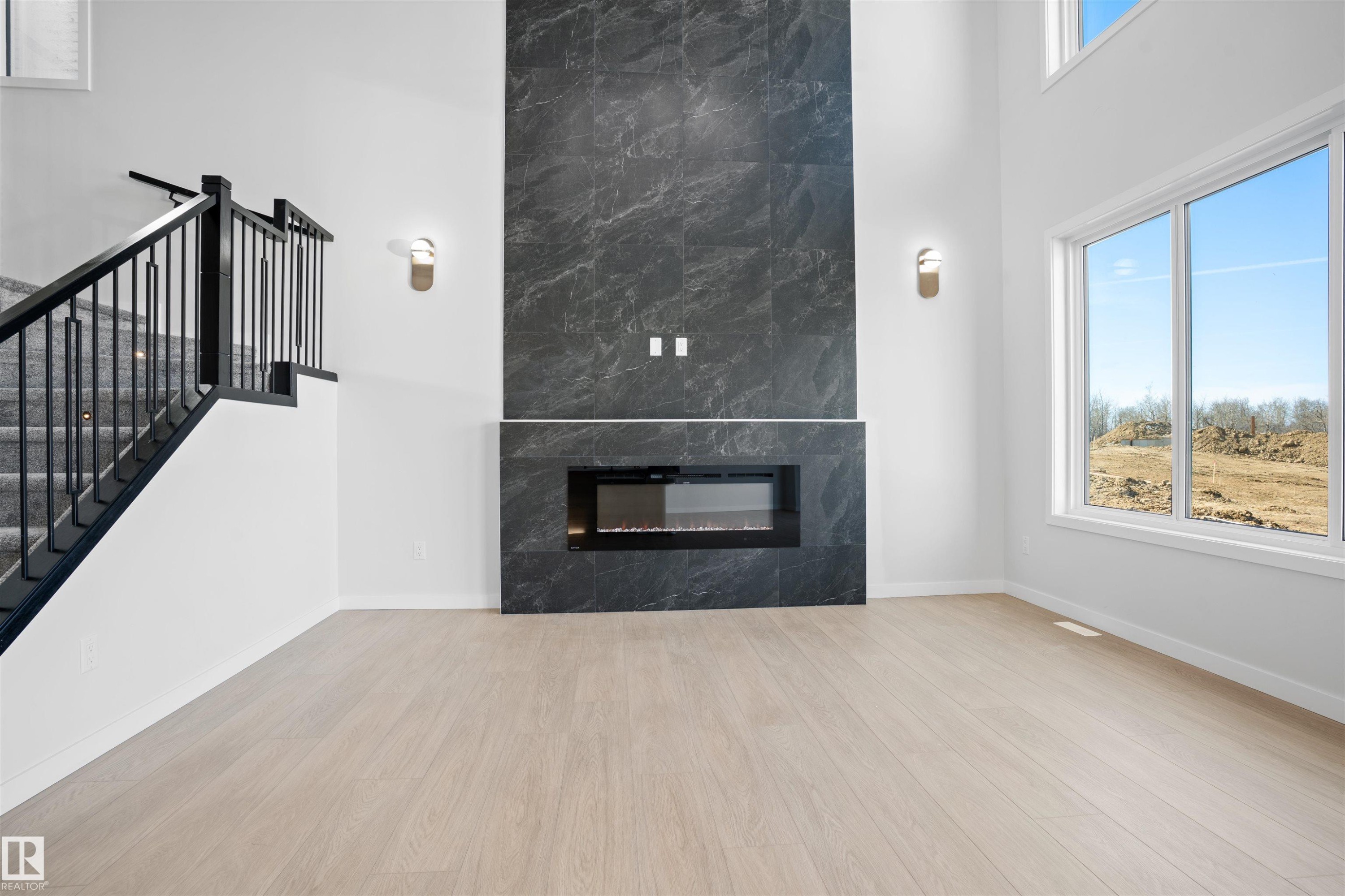 Soaring ceilings with a full-height dark stone fireplace surround and integrated linear electric fireplace - 1849 Crossbill Loop Nw, Edmonton, AB - Indoor Photo Showing Other Room With Fireplace
