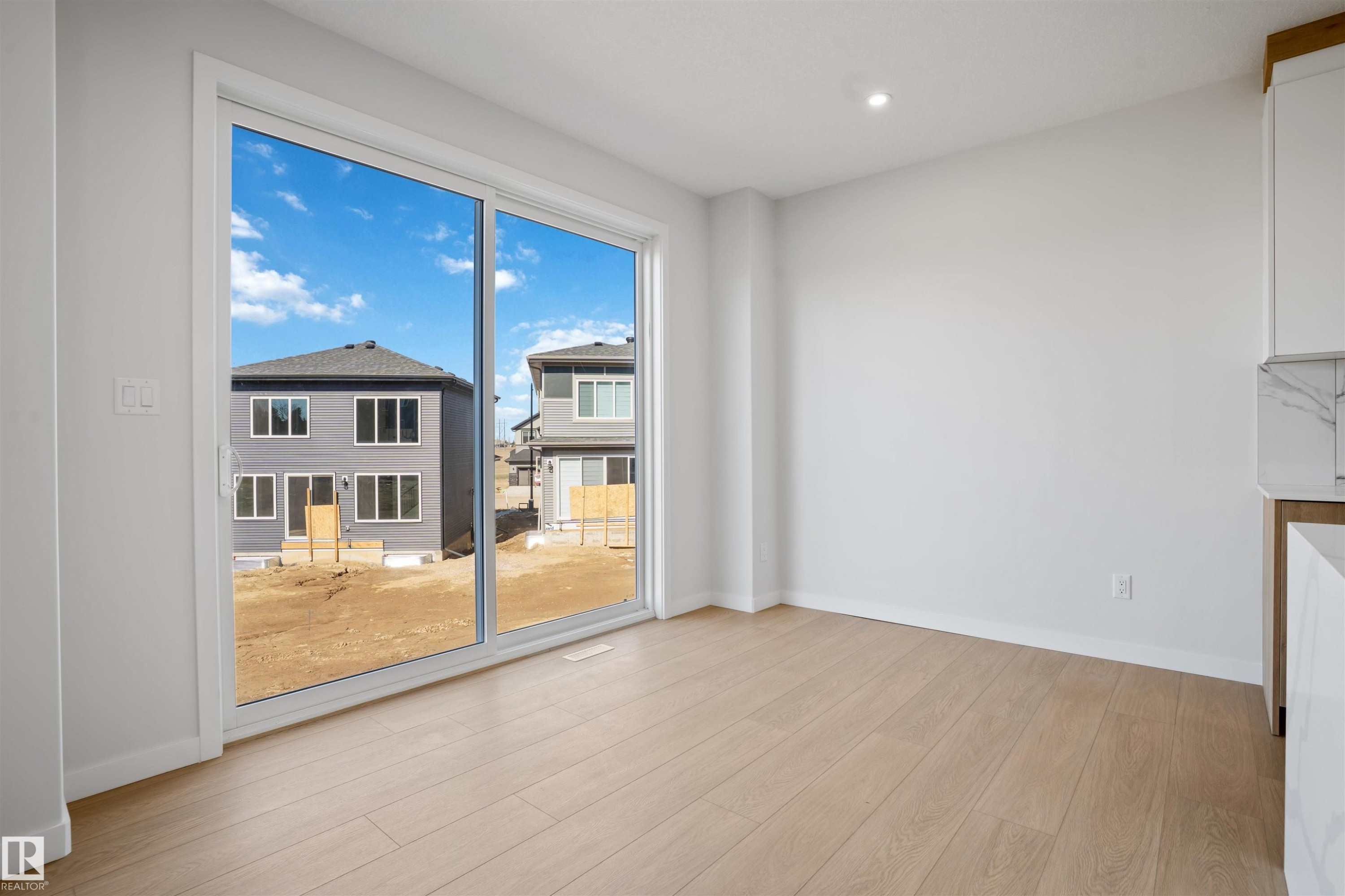 Sliding glass door opening to an exterior space with light wood-finish flooring, white baseboards, and neutral wall tones - 1849 Crossbill Loop Nw, Edmonton, AB - Indoor Photo Showing Other Room
