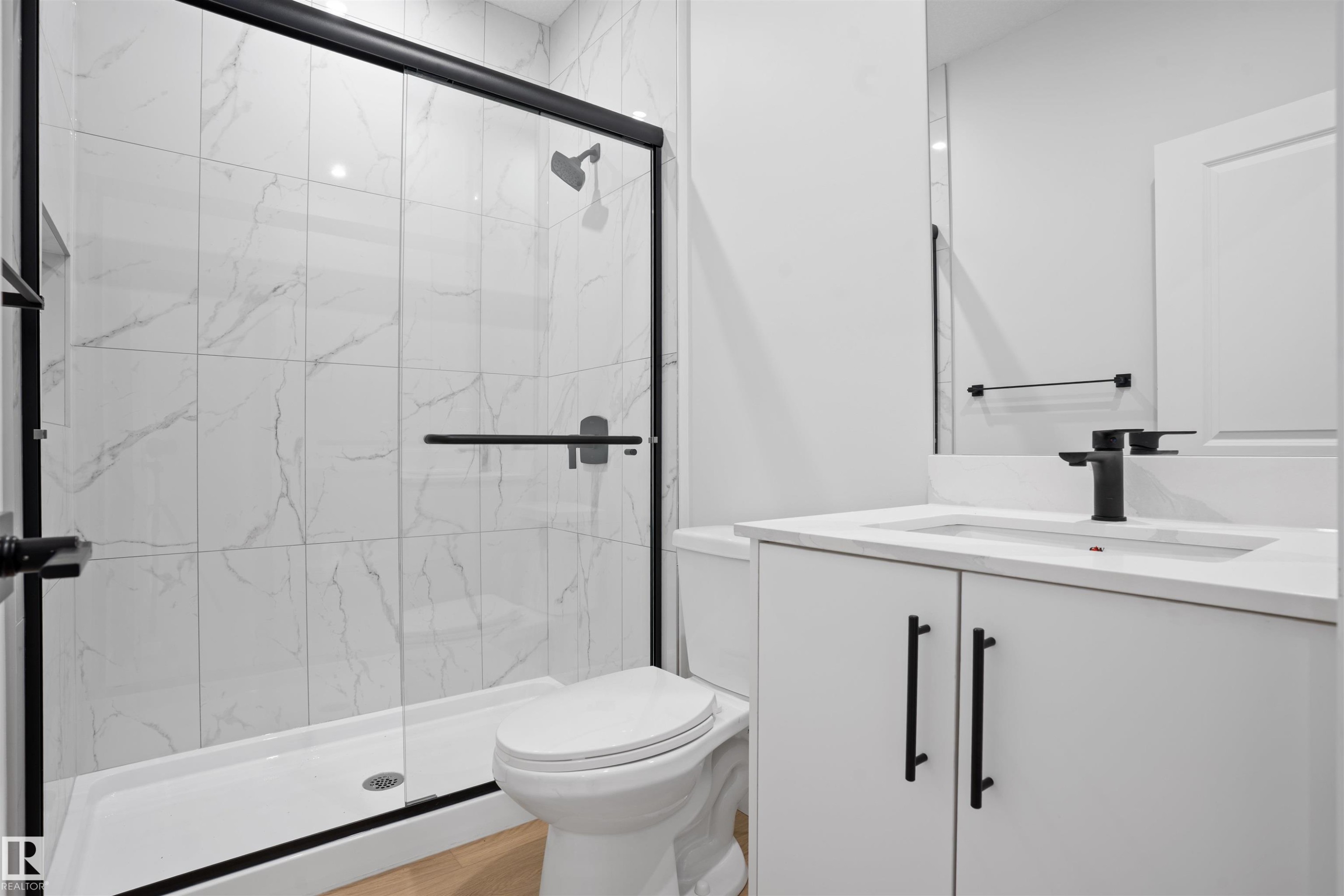 Walk-in shower with clear glass enclosure, matte black hardware, and large format white tile with grey veining - 1849 Crossbill Loop Nw, Edmonton, AB - Indoor Photo Showing Bathroom