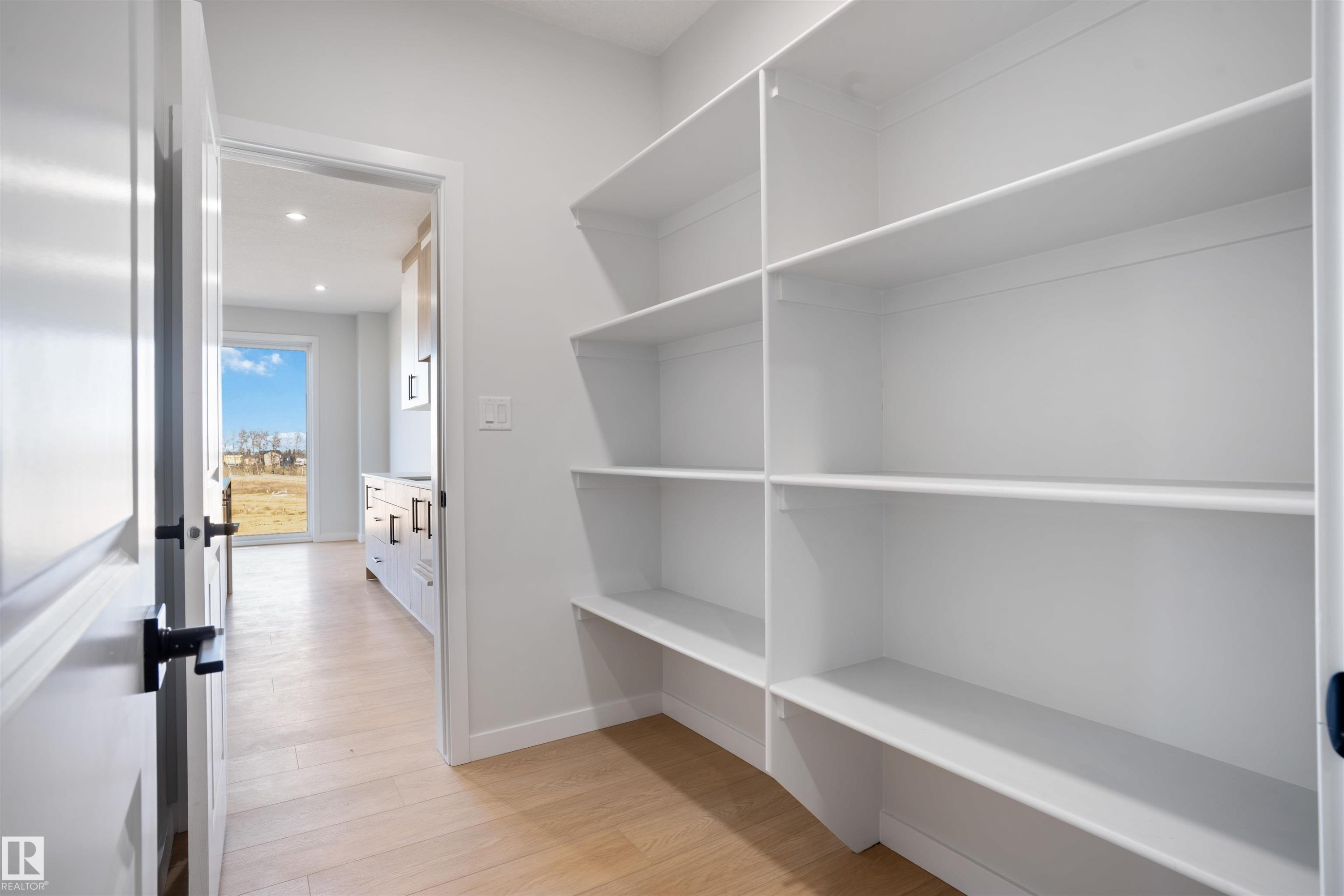 Spacious pantry with multiple built-in white shelving units, light wood-finish flooring, and white trim - 1849 Crossbill Loop Nw, Edmonton, AB - Indoor With Storage
