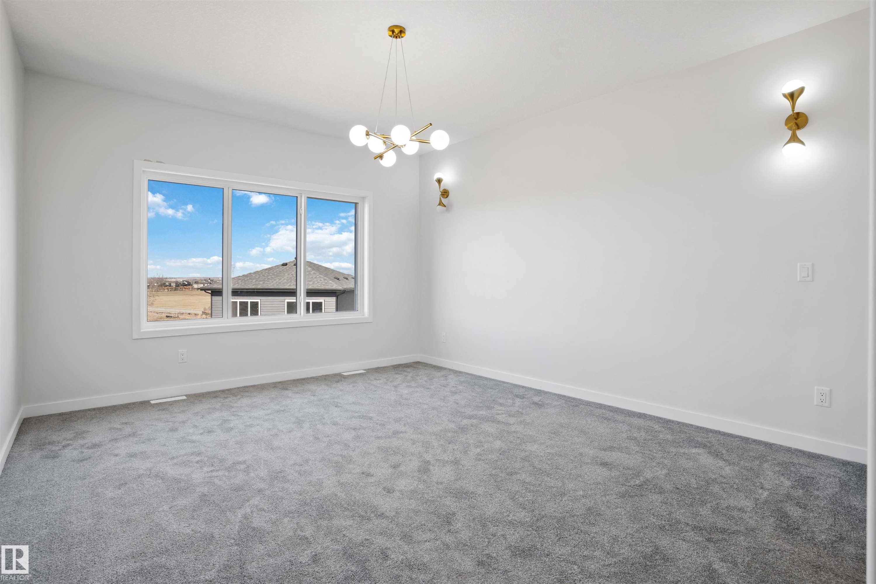 Spacious room featuring a multi-pane window, modern gold-tone chandelier, and coordinating wall sconces - 1849 Crossbill Loop Nw, Edmonton, AB - Indoor Photo Showing Other Room
