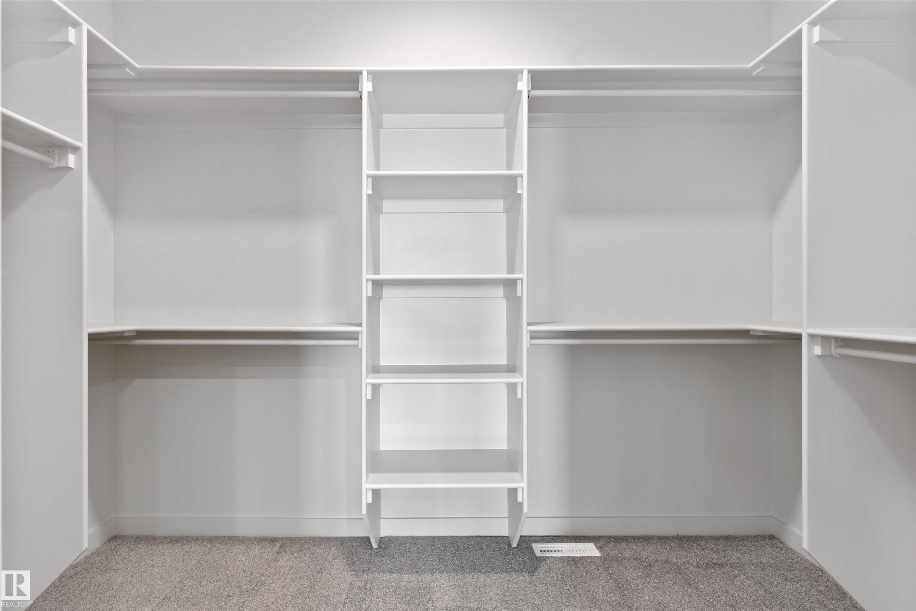 Spacious custom closet system featuring white shelving, multiple hanging rods, built-in cubbies, and light gray carpeting - 1849 Crossbill Loop Nw, Edmonton, AB - Indoor With Storage