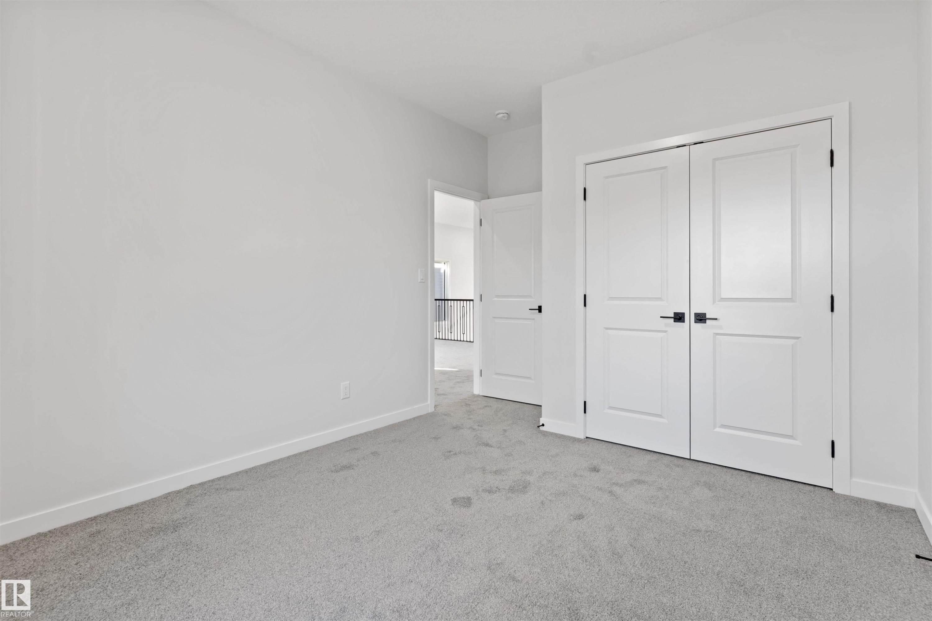 Light gray carpeting complementing white walls, trim, and solid core doors with matte black hardware - 1849 Crossbill Loop Nw, Edmonton, AB - Indoor Photo Showing Other Room