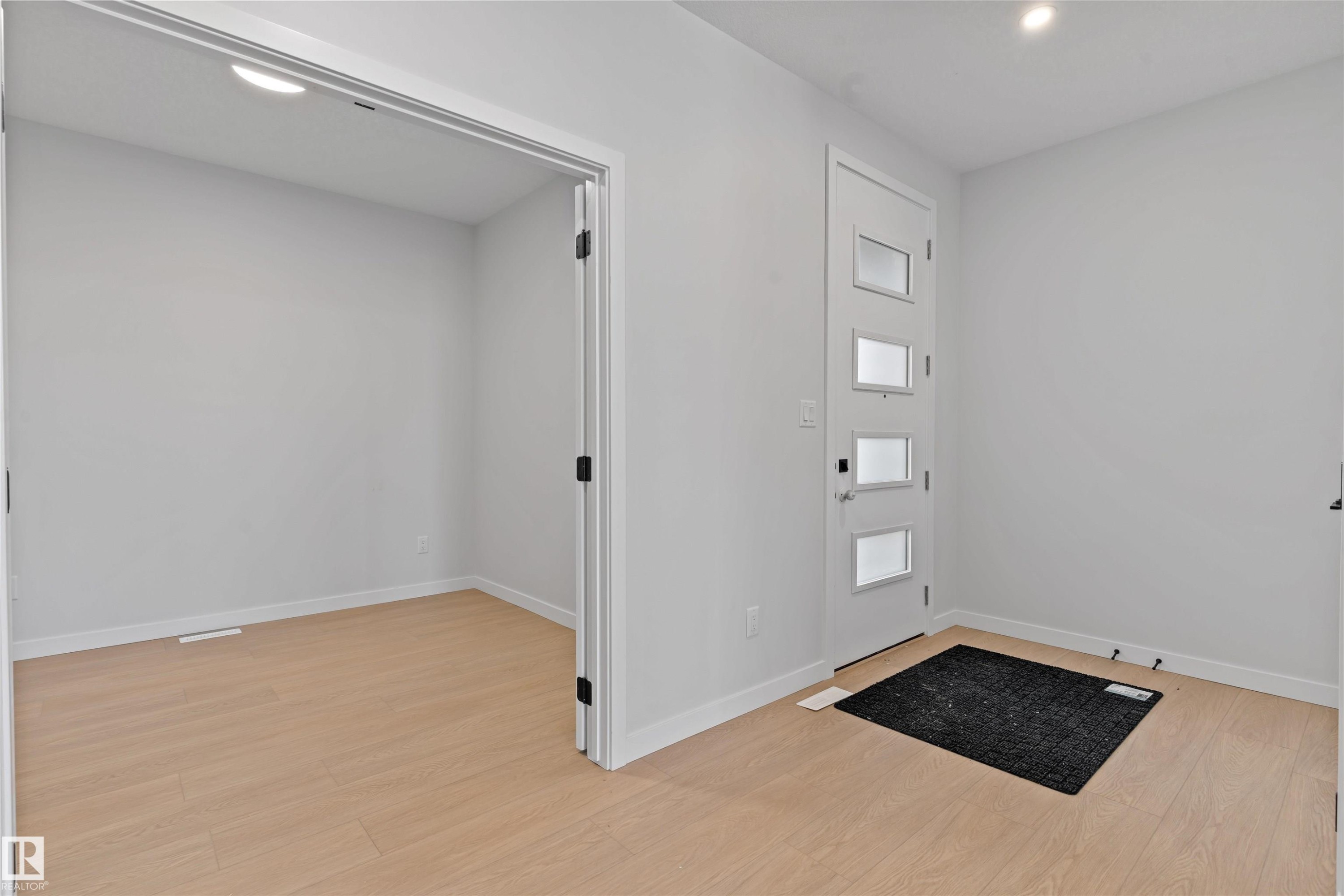 Entryway featuring a modern door with four rectangular glass inserts, light wood-finish flooring, white baseboards, and neutral wall paint - 1849 Crossbill Loop Nw, Edmonton, AB - Indoor Photo Showing Other Room