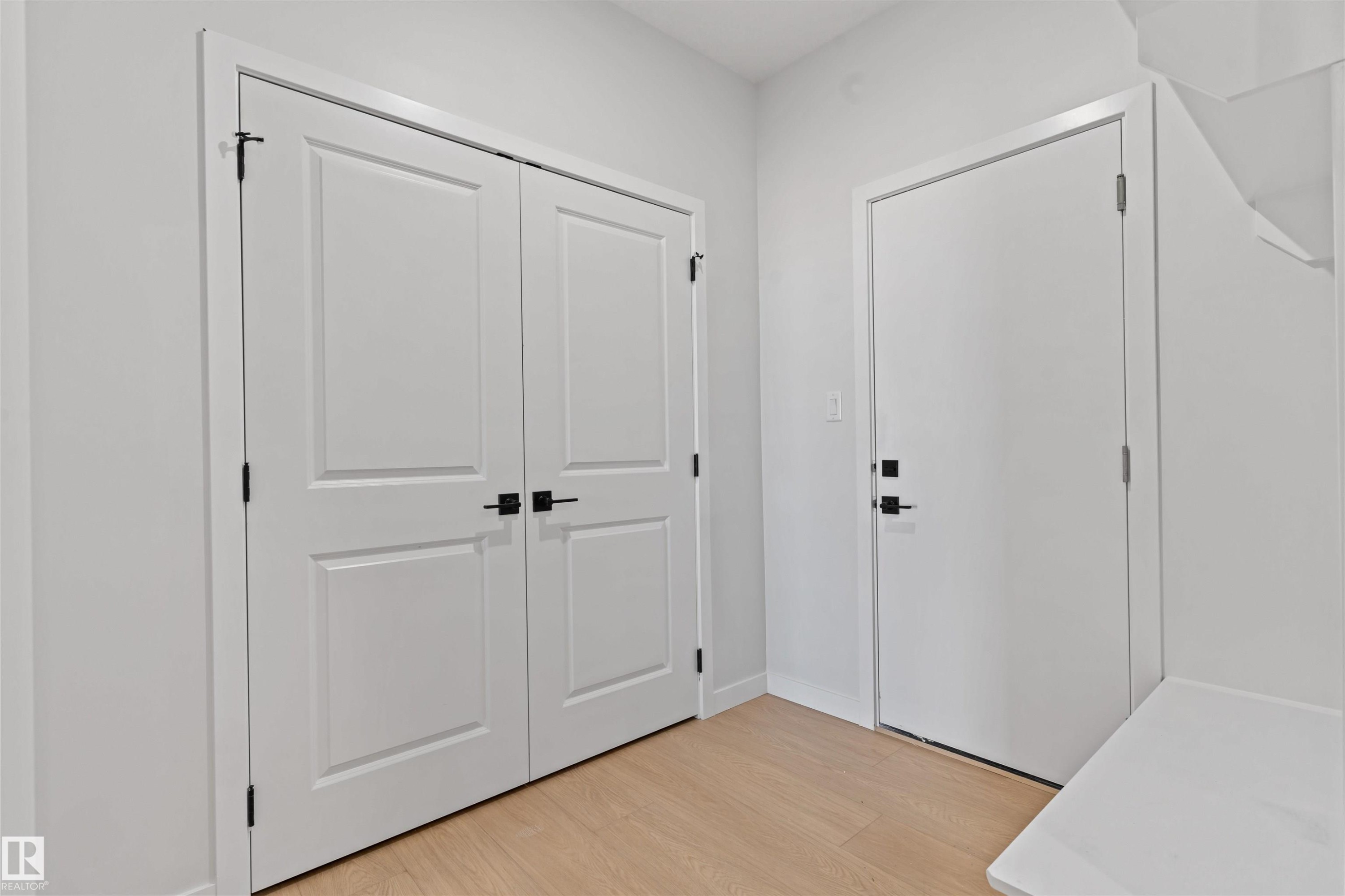 Entryway featuring light wood-finish flooring, white walls, and a pair of double panel doors with matte black hardware - 1849 Crossbill Loop Nw, Edmonton, AB - Indoor Photo Showing Other Room