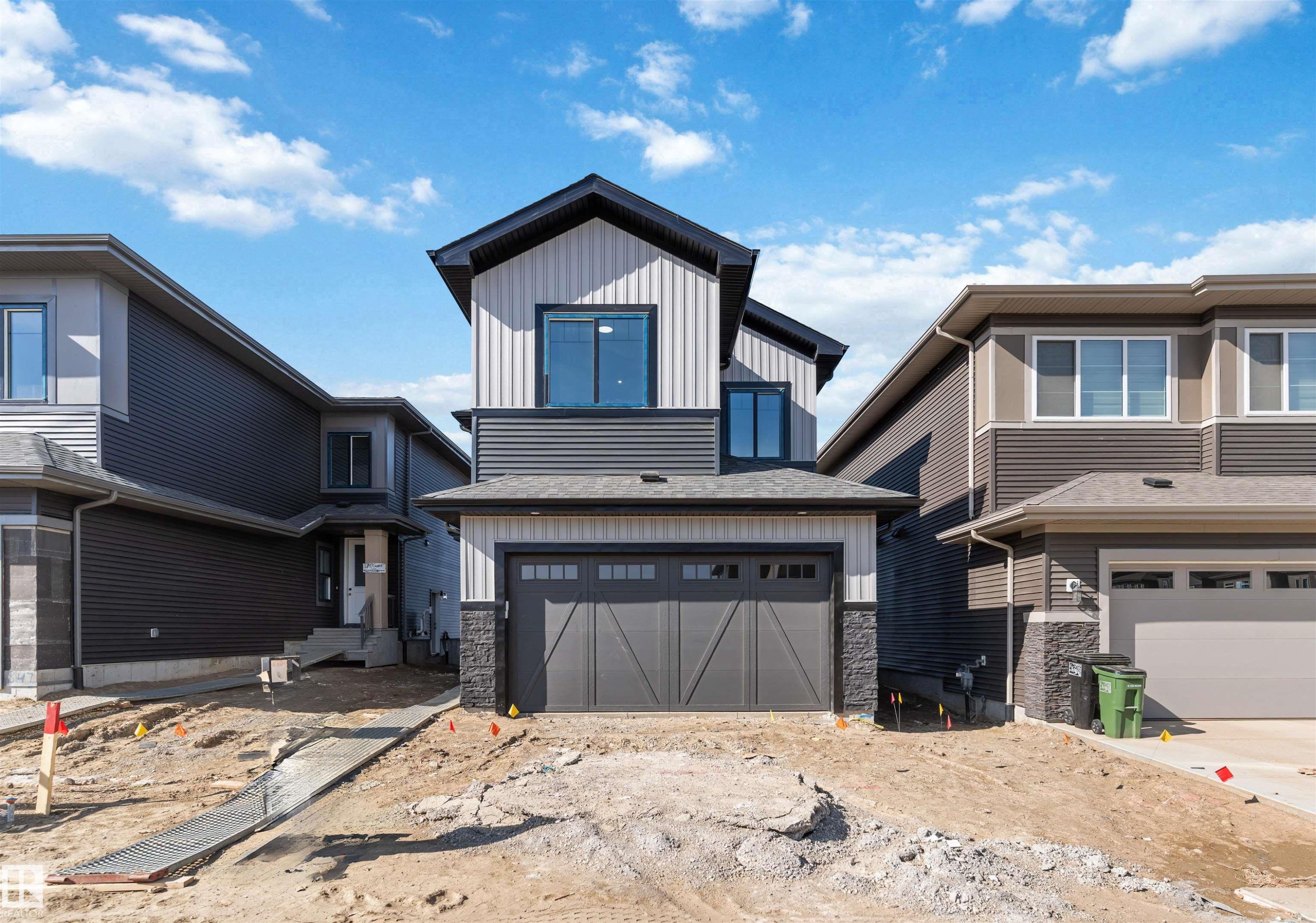 Modern two-story residence featuring a dark gray garage door, vertical and horizontal siding in shades of gray, black trim accents, and a stone facade detail - 1849 Crossbill Loop Nw, Edmonton, AB - Outdoor With Facade