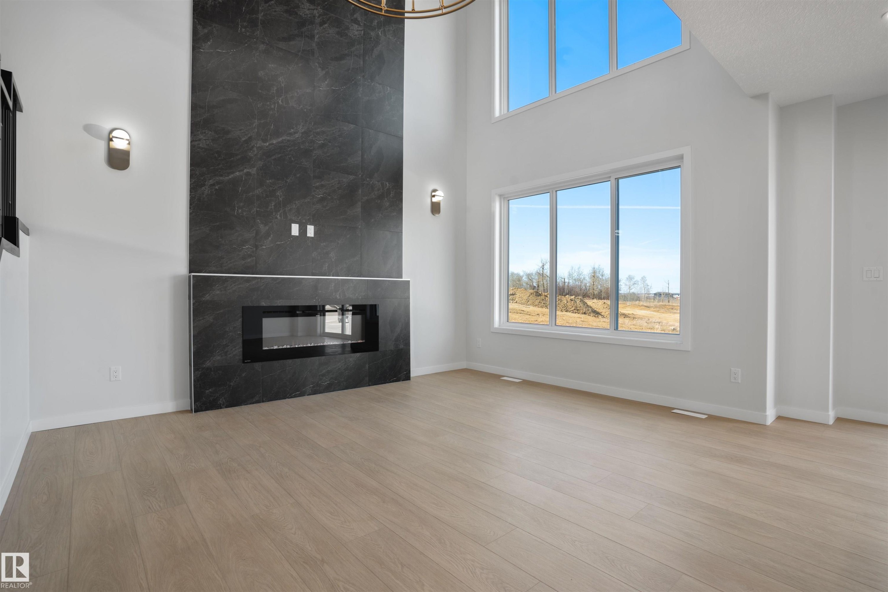 Spacious room featuring a floor-to-ceiling fireplace with dark stone-finish tile, light wood-finish flooring, and large windows - 1849 Crossbill Loop Nw, Edmonton, AB - Indoor Photo Showing Living Room With Fireplace
