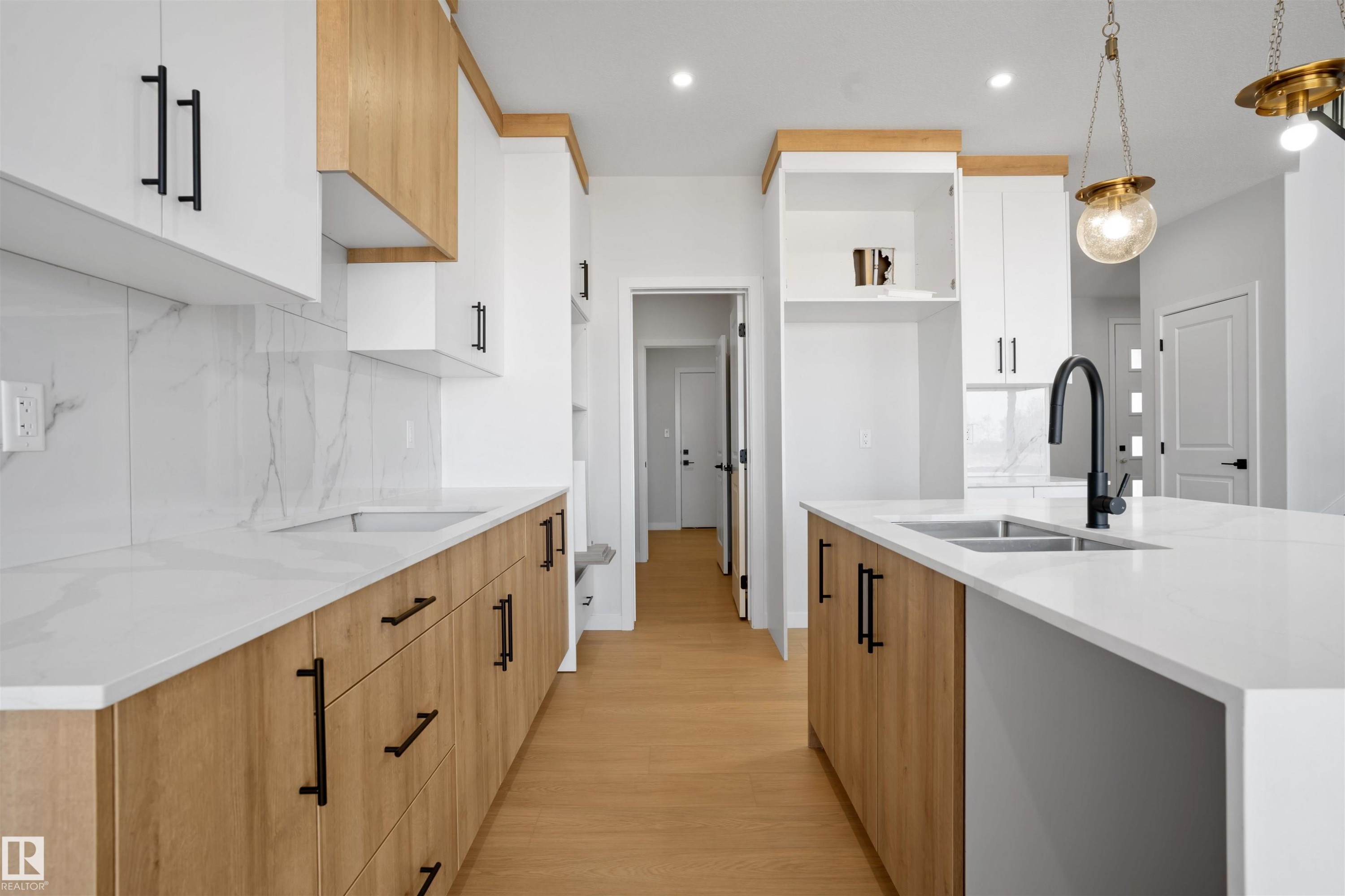 Contemporary kitchen featuring a large center island with integrated sink, sleek white countertops, and a striking two-tone cabinet design - 1849 Crossbill Loop Nw, Edmonton, AB - Indoor Photo Showing Kitchen With Double Sink With Upgraded Kitchen
