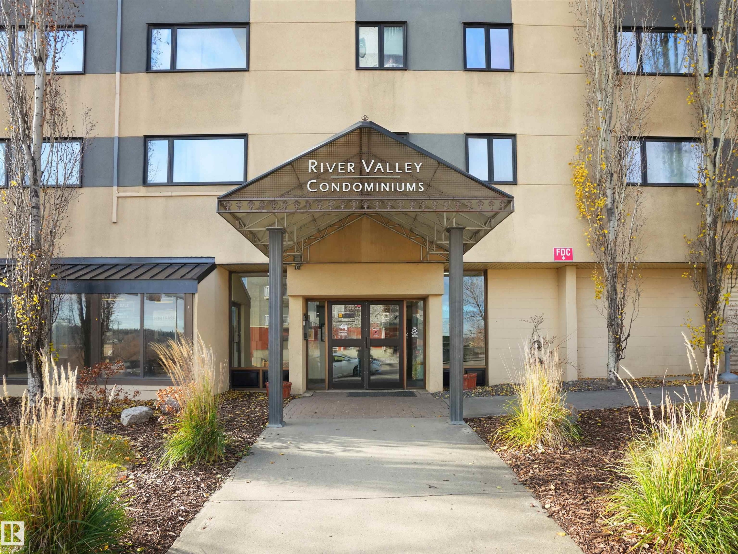 "River Valley Condominiums" exterior featuring a covered entry, established landscaping, and multi-story construction - #307 9710 105 St Nw, Edmonton, AB - Outdoor With Facade