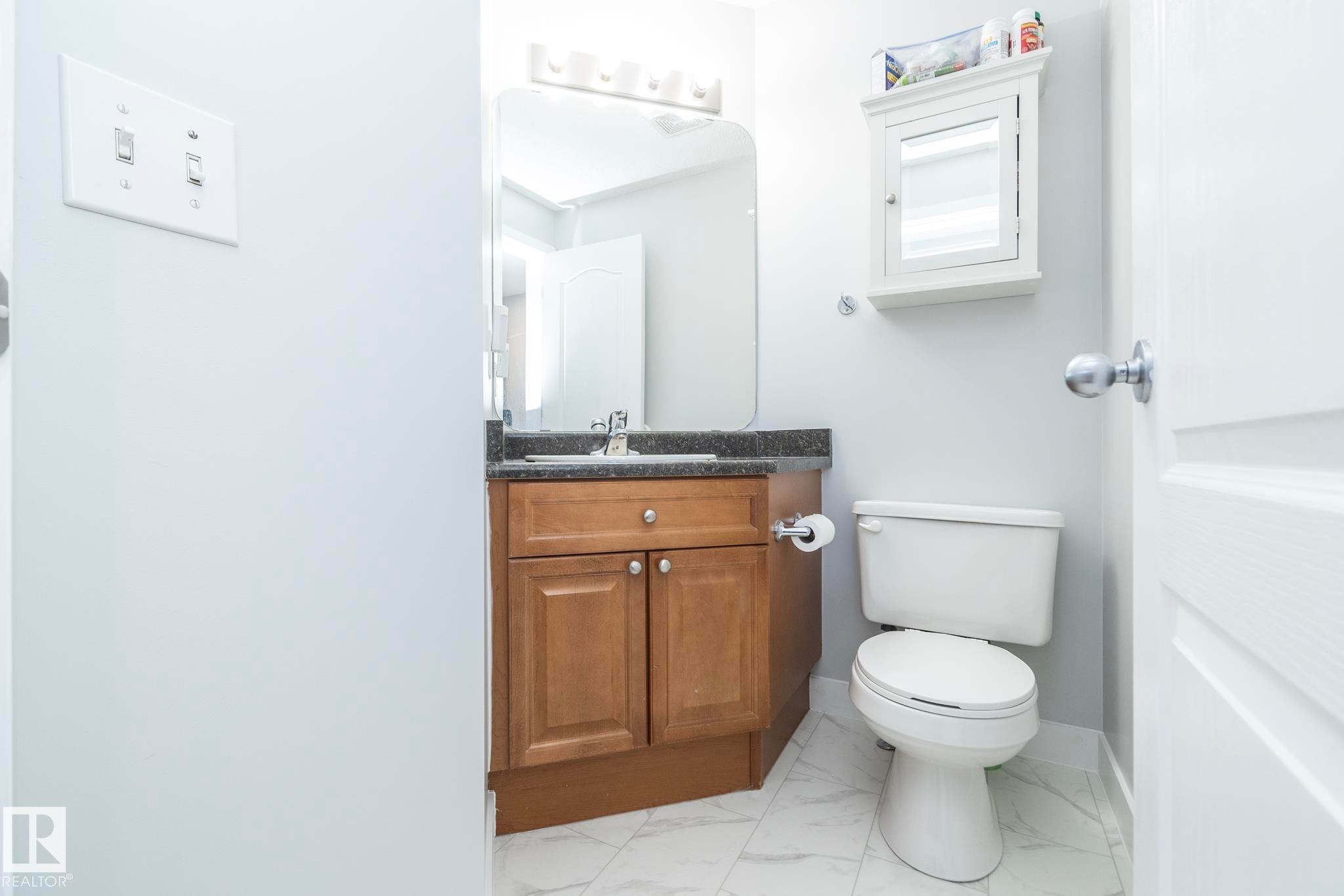 Bathroom featuring a wood-finish vanity with a dark countertop and undermount sink, a wall-mounted mirror, and tile flooring - 65 Birchmont Drive, Leduc, AB - Indoor Photo Showing Bathroom
