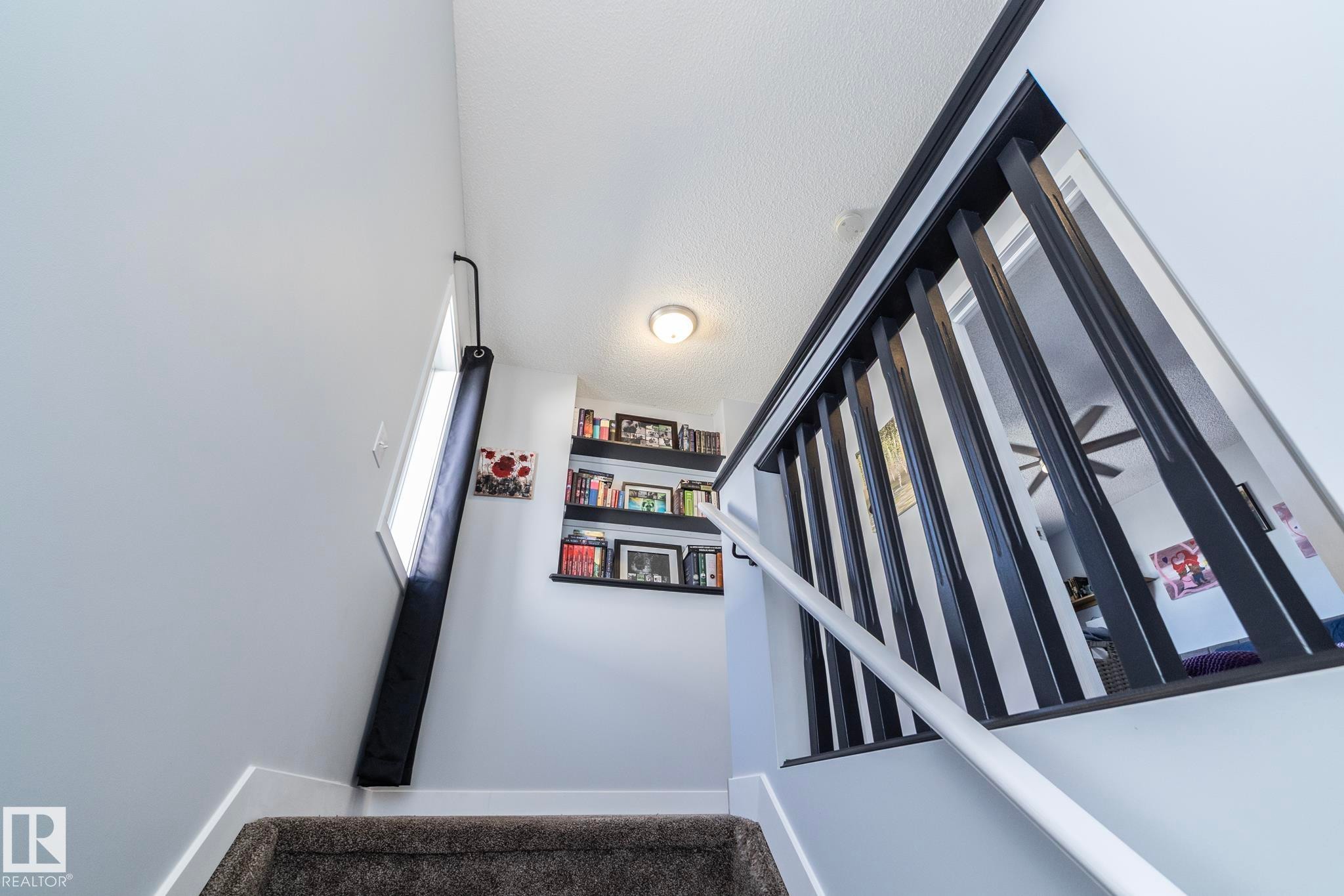 Carpeted staircase featuring a modern black baluster railing and a white handrail - 65 Birchmont Drive, Leduc, AB - Indoor Photo Showing Other Room