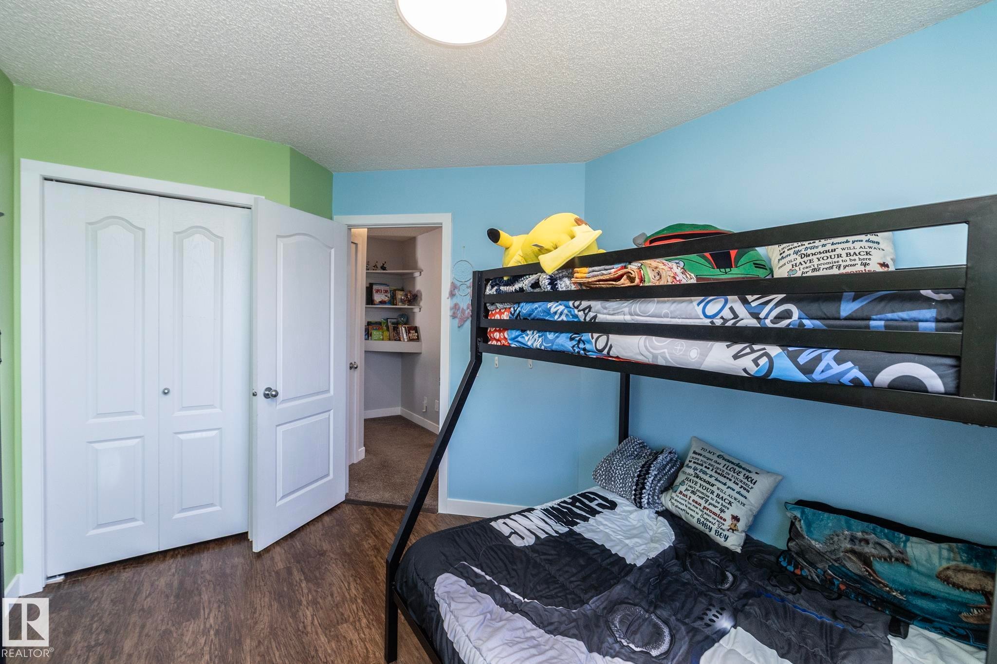 Room featuring wood-finish flooring, a white bi-fold closet, a standard white door, and a recessed ceiling light - 65 Birchmont Drive, Leduc, AB - Indoor Photo Showing Bedroom