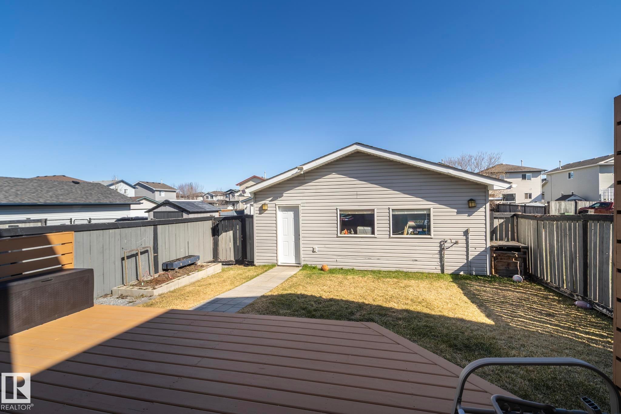 Expansive backyard featuring a composite deck, a detached garage with siding exterior, a concrete walkway, and a perimeter fence - 65 Birchmont Drive, Leduc, AB - Outdoor With Exterior