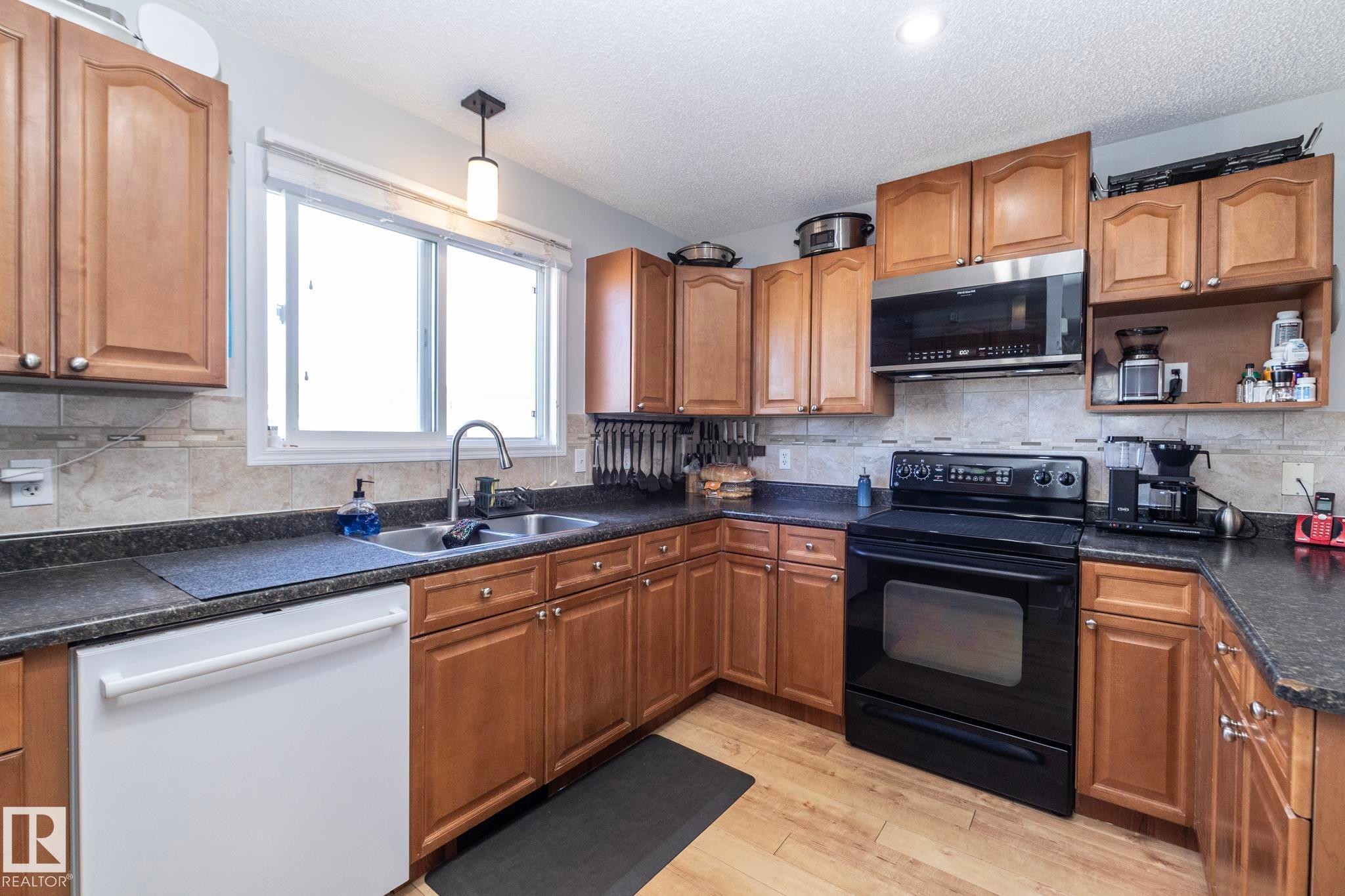 Kitchen featuring wood cabinetry, dark countertops, a double basin sink, and a black range with an above-range microwave - 65 Birchmont Drive, Leduc, AB - Indoor Photo Showing Kitchen With Double Sink