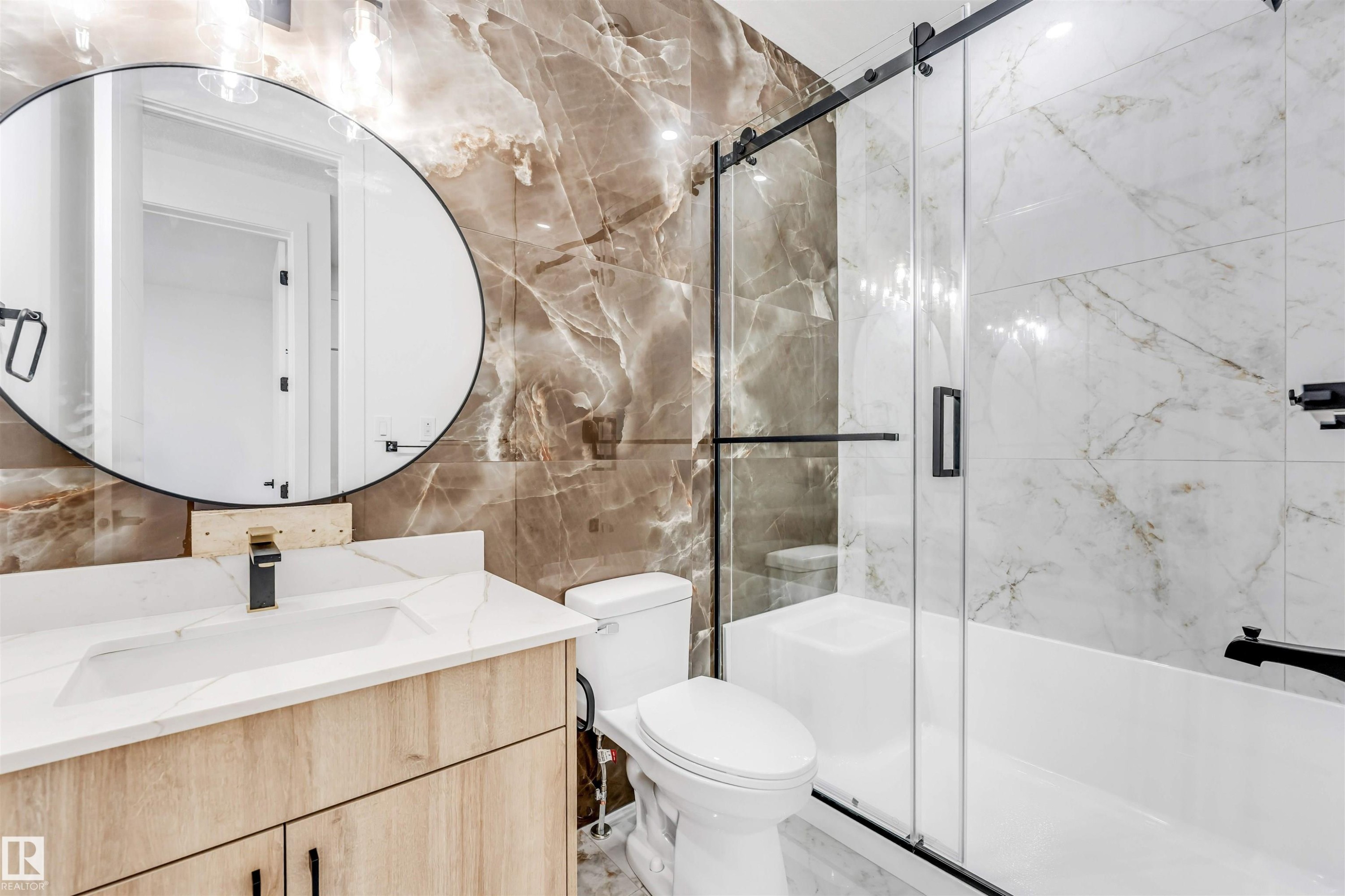 Modern bathroom featuring a wood-finish vanity with a white countertop and integrated sink, a large circular mirror, and a black-finish faucet - 4006 35 St, Beaumont, AB - Indoor Photo Showing Bathroom
