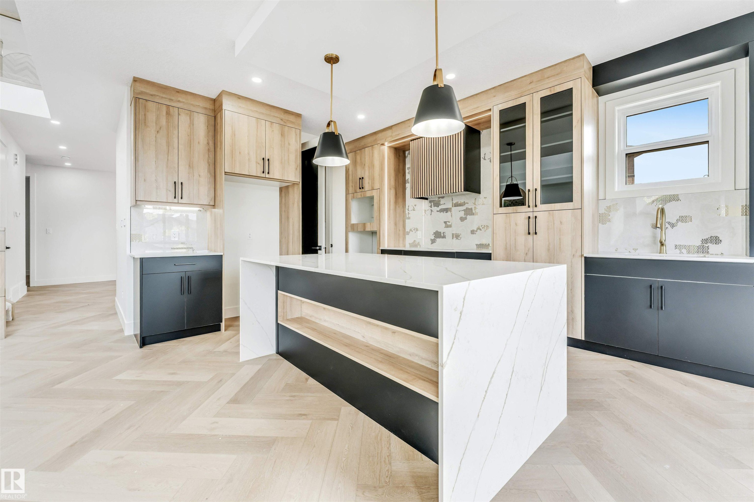Contemporary kitchen featuring a waterfall island with integrated shelving, herringbone wood-finish flooring, two-tone cabinetry, and a unique backsplash with a gold-tone faucet - 4006 35 St, Beaumont, AB - Indoor Photo Showing Kitchen