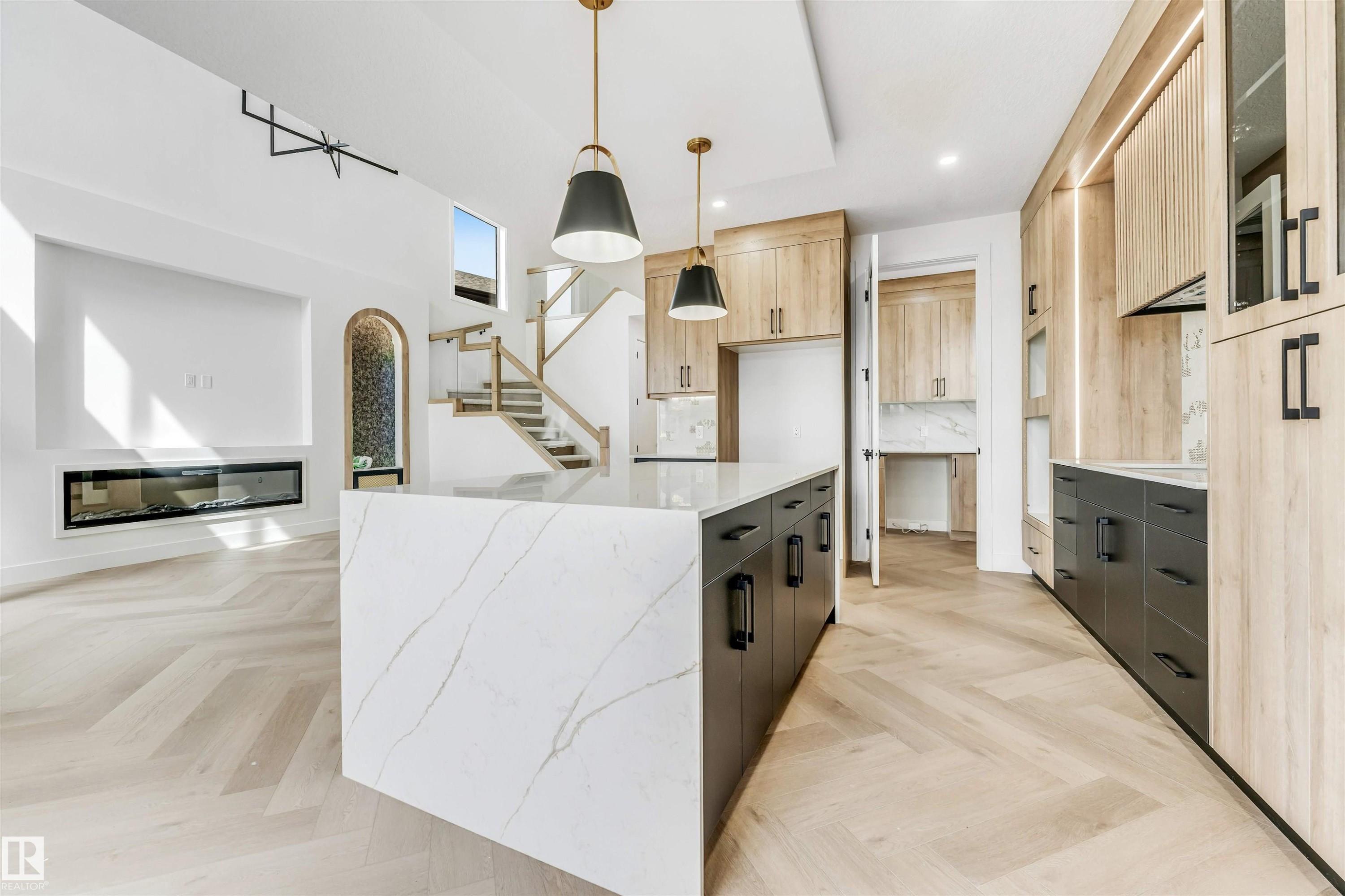 Open-concept living space featuring herringbone wood-finish flooring, a contemporary linear fireplace, and a kitchen island with a waterfall countertop - 4006 35 St, Beaumont, AB - Indoor Photo Showing Kitchen