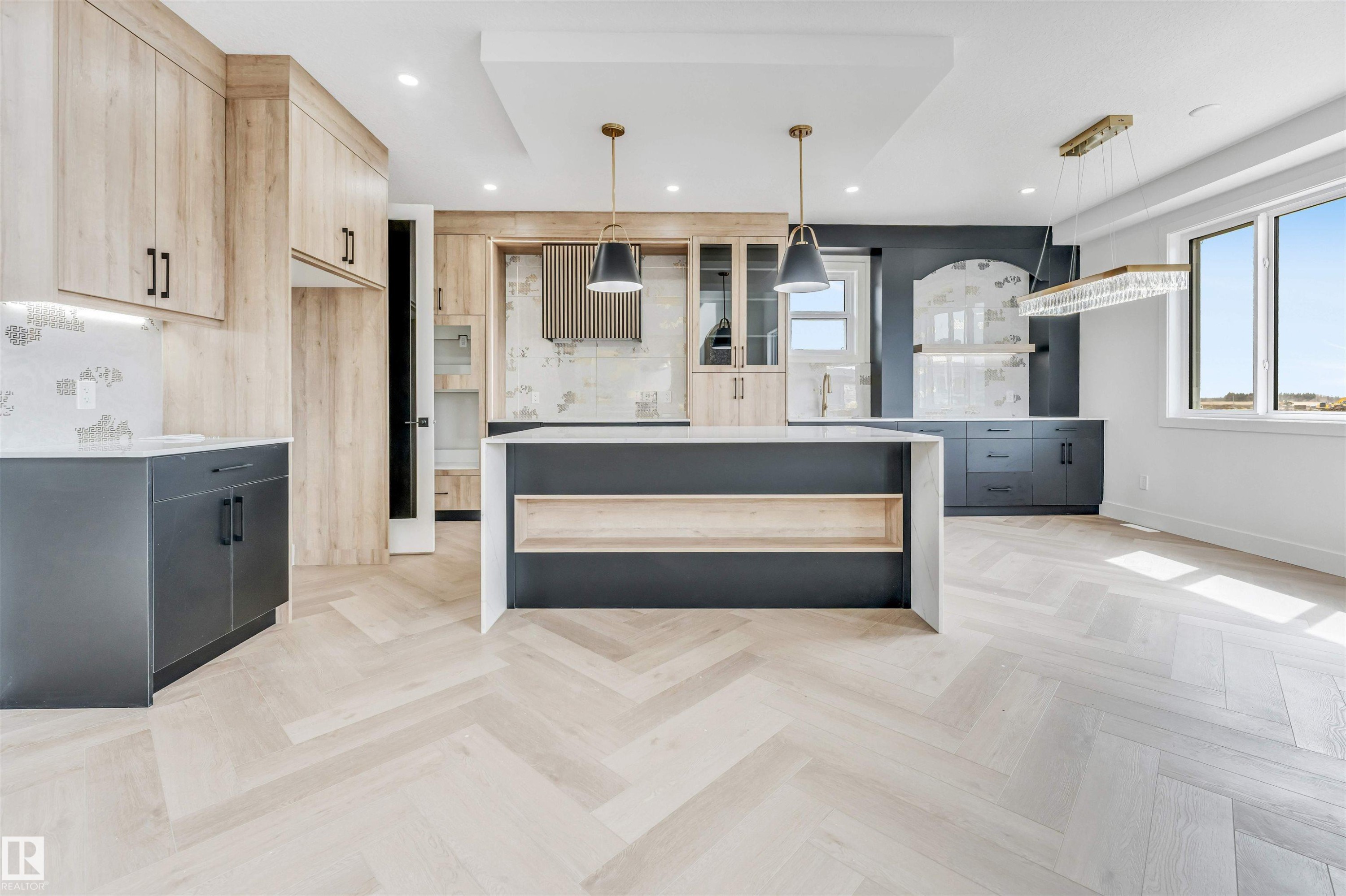 Spacious kitchen featuring light wood-finish herringbone flooring, a large island with integrated shelving, and dark lower cabinetry - 4006 35 St, Beaumont, AB - Indoor