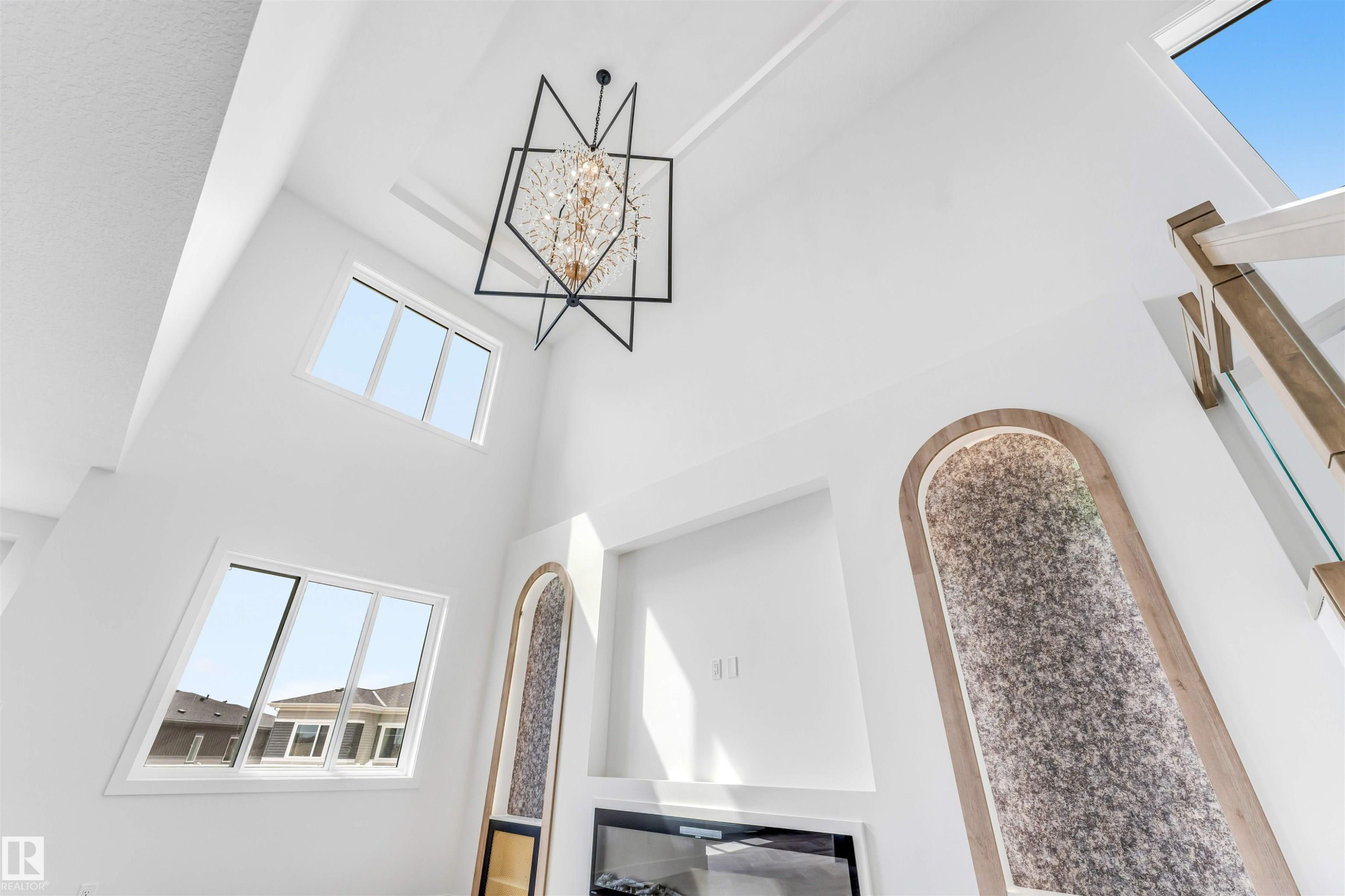 Two-story living space featuring a geometric chandelier, dual-level windows, and an integrated electric fireplace - 4006 35 St, Beaumont, AB - Indoor Photo Showing Other Room