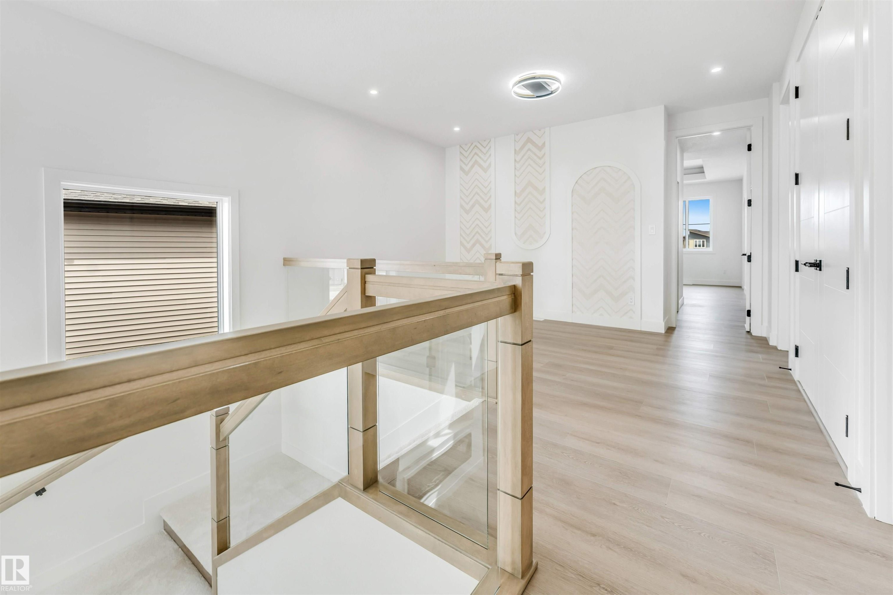 Upper-level landing featuring wood-finish flooring, glass panel railing, recessed lighting, decorative wall panels, and white paneled doors with matte black hardware - 4006 35 St, Beaumont, AB - Indoor Photo Showing Other Room
