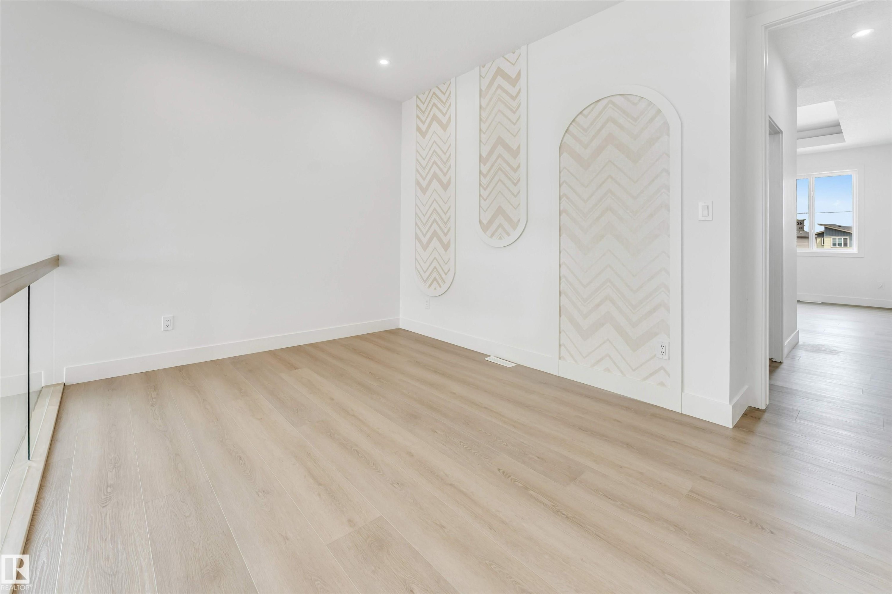 Contemporary interior featuring light wood-finish flooring, recessed lighting, and a white accent wall with decorative chevron paneling - 4006 35 St, Beaumont, AB - Indoor Photo Showing Other Room