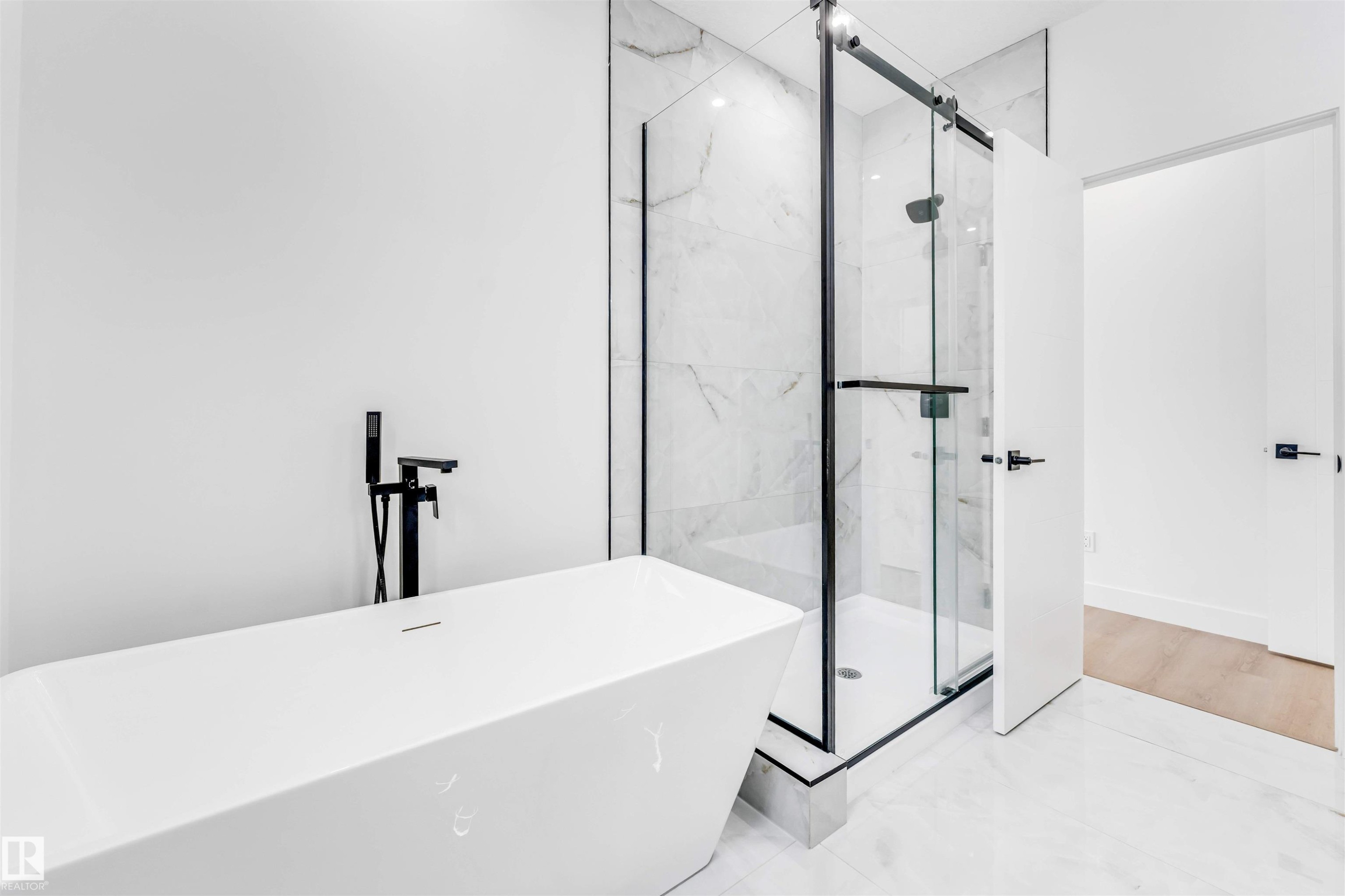 Contemporary bathroom featuring a freestanding soaking tub with matte black floor-mounted filler, a glass-enclosed shower with matte black hardware, and large format white tile flooring - 4006 35 St, Beaumont, AB - Indoor Photo Showing Bathroom