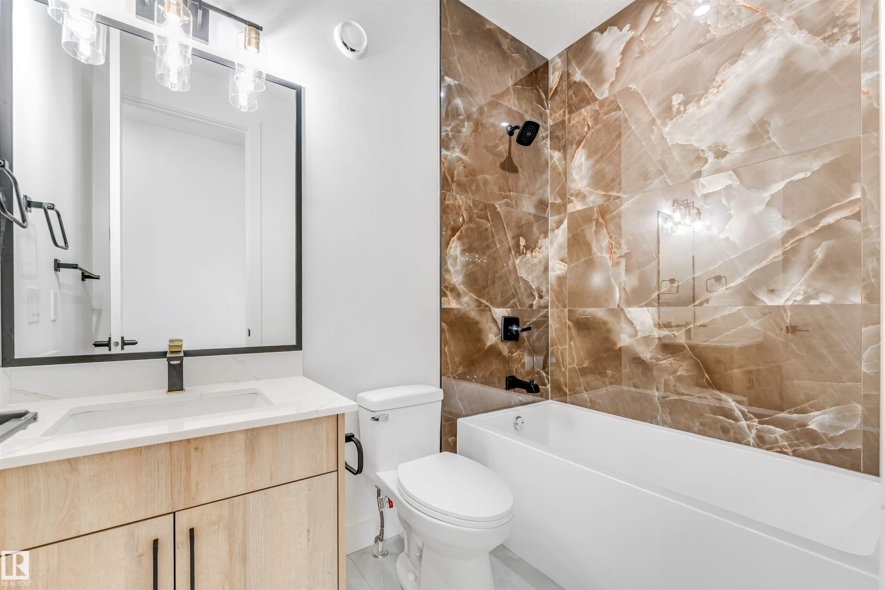Bathroom featuring a built-in tub with brown marble-look tile surround, a light wood-finish vanity with a white countertop, and a black-framed mirror with overhead lighting - 4006 35 St, Beaumont, AB - Indoor Photo Showing Bathroom