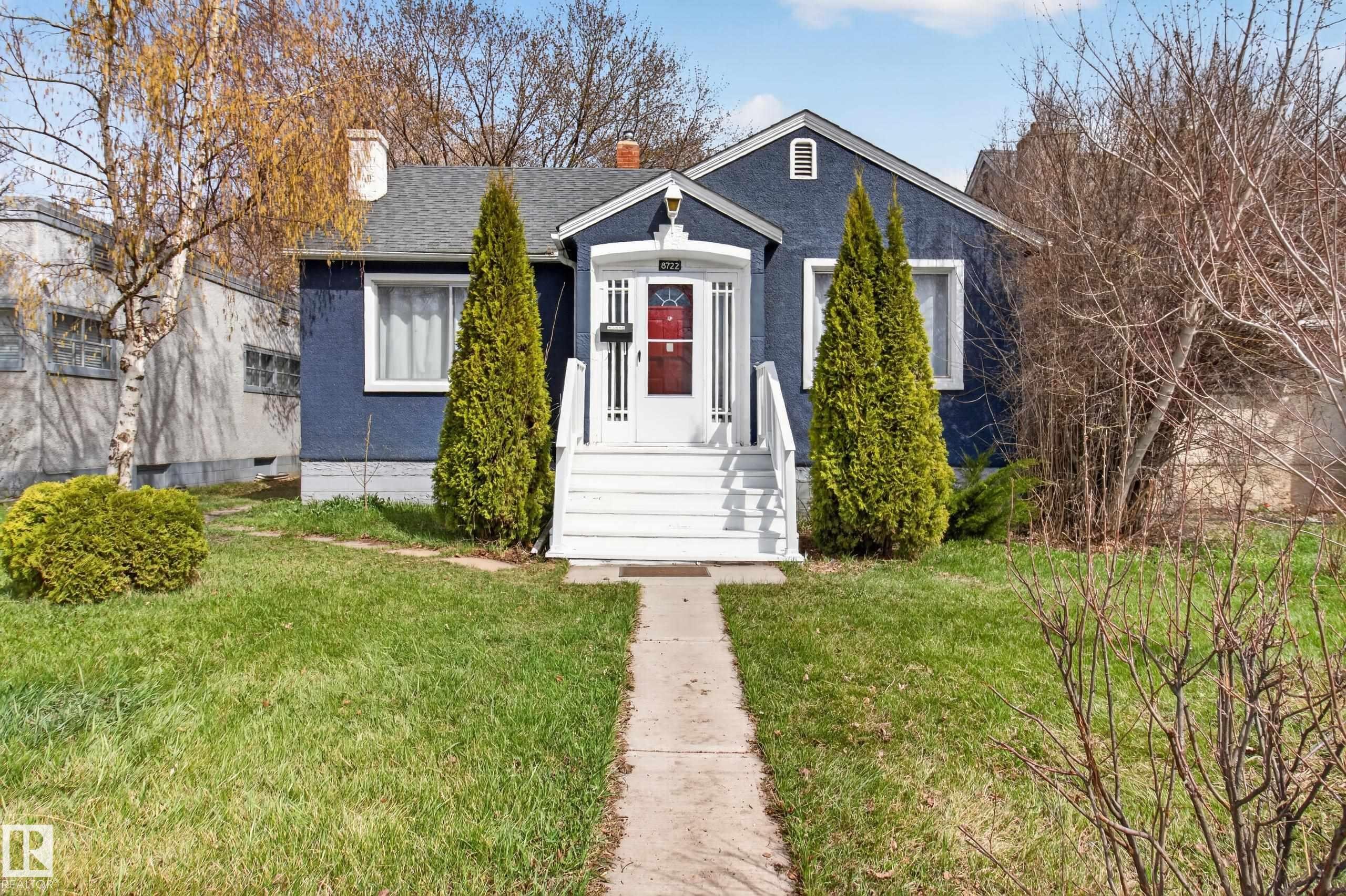 Cottage-style residence featuring a dark blue exterior, white trim, and a prominent front porch with white railings - 8722 112 Avenue, Edmonton, AB - Outdoor With Facade