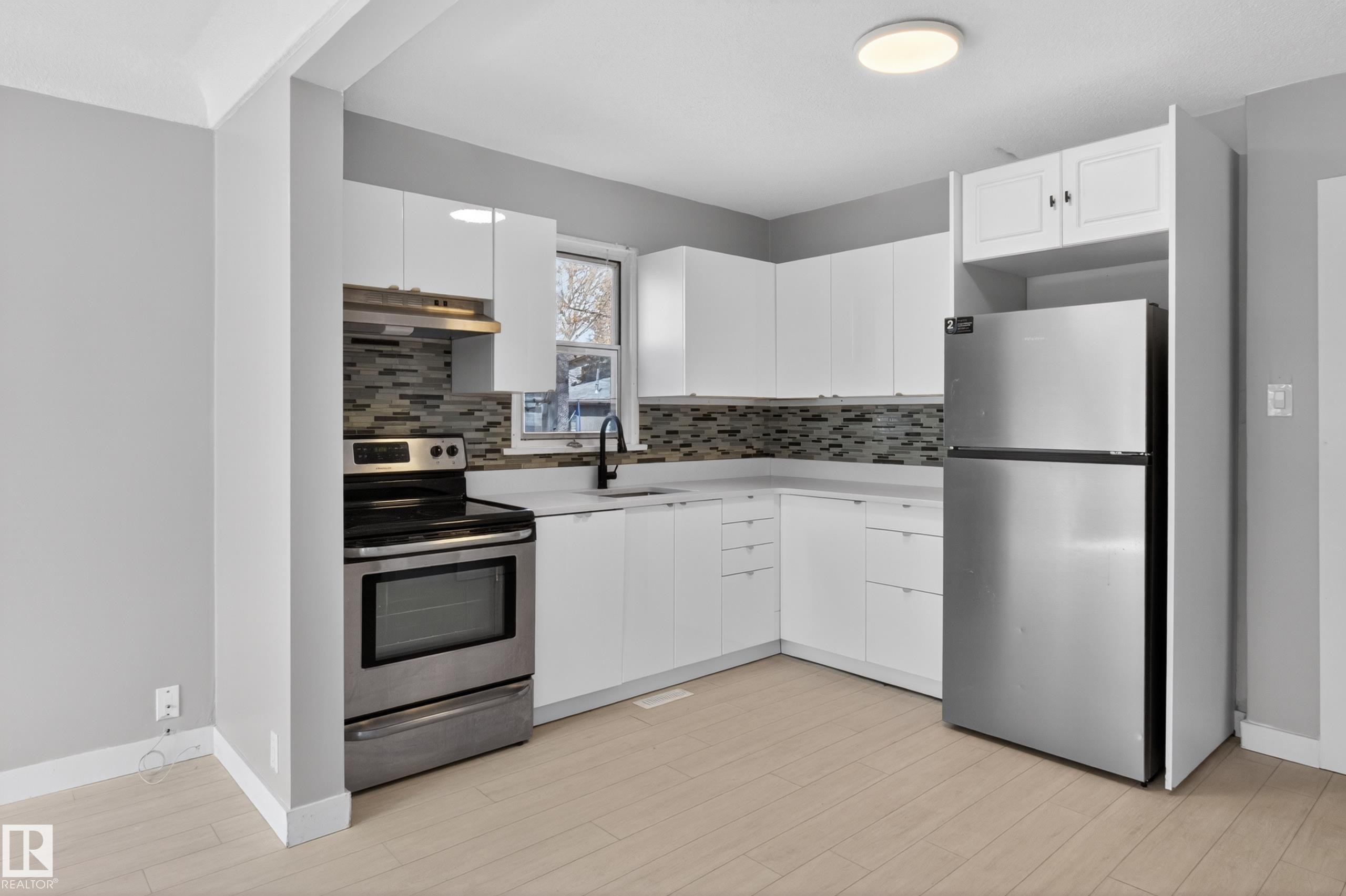 Kitchen featuring white cabinetry, stainless steel appliances, a mosaic tile backsplash, a matte black faucet, and wood-finish flooring - 8722 112 Avenue, Edmonton, AB - Indoor Photo Showing Kitchen
