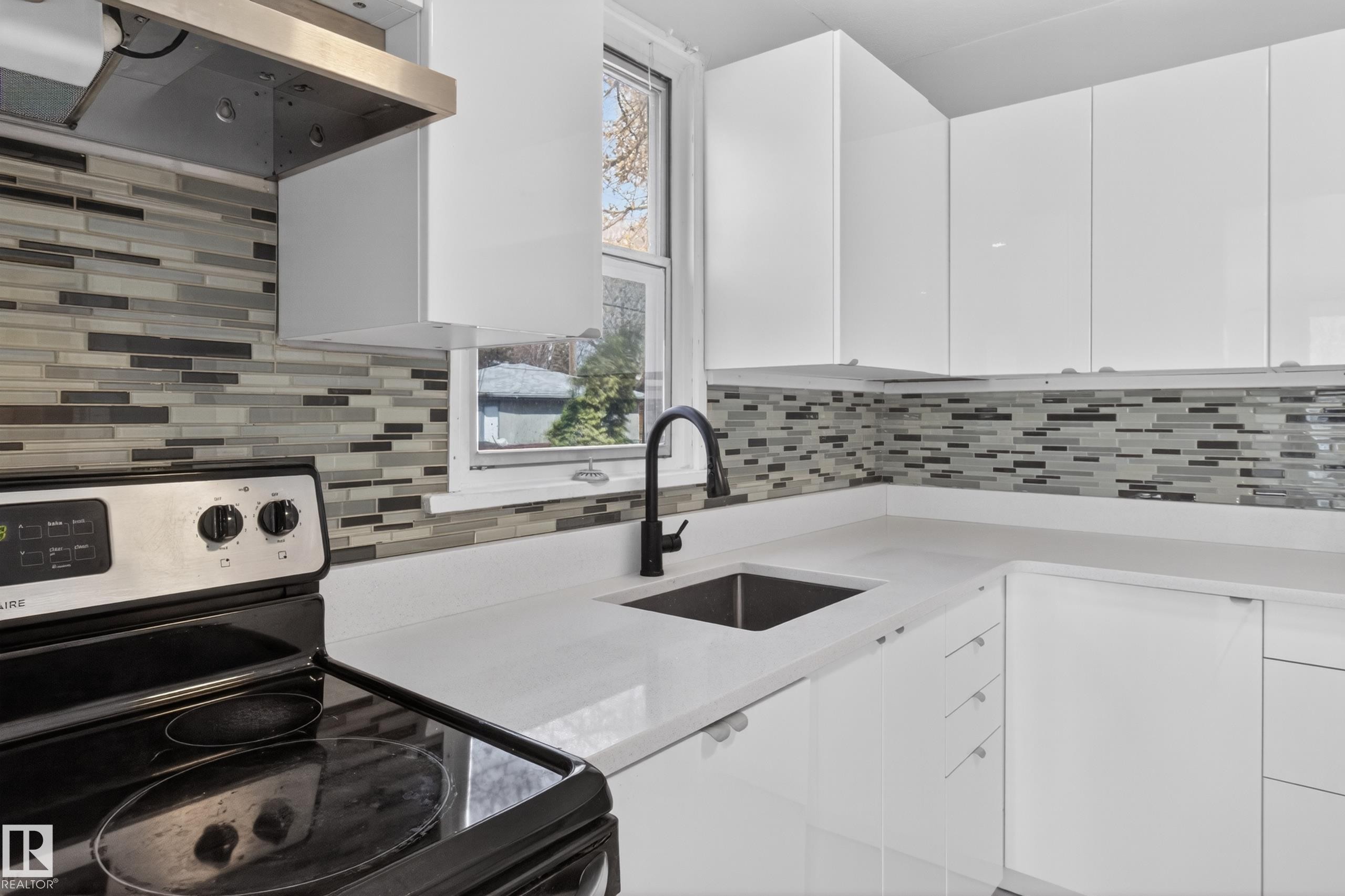 Modern kitchen featuring white cabinetry, a mosaic tile backsplash, and light-colored countertops - 8722 112 Avenue, Edmonton, AB - Indoor Photo Showing Kitchen
