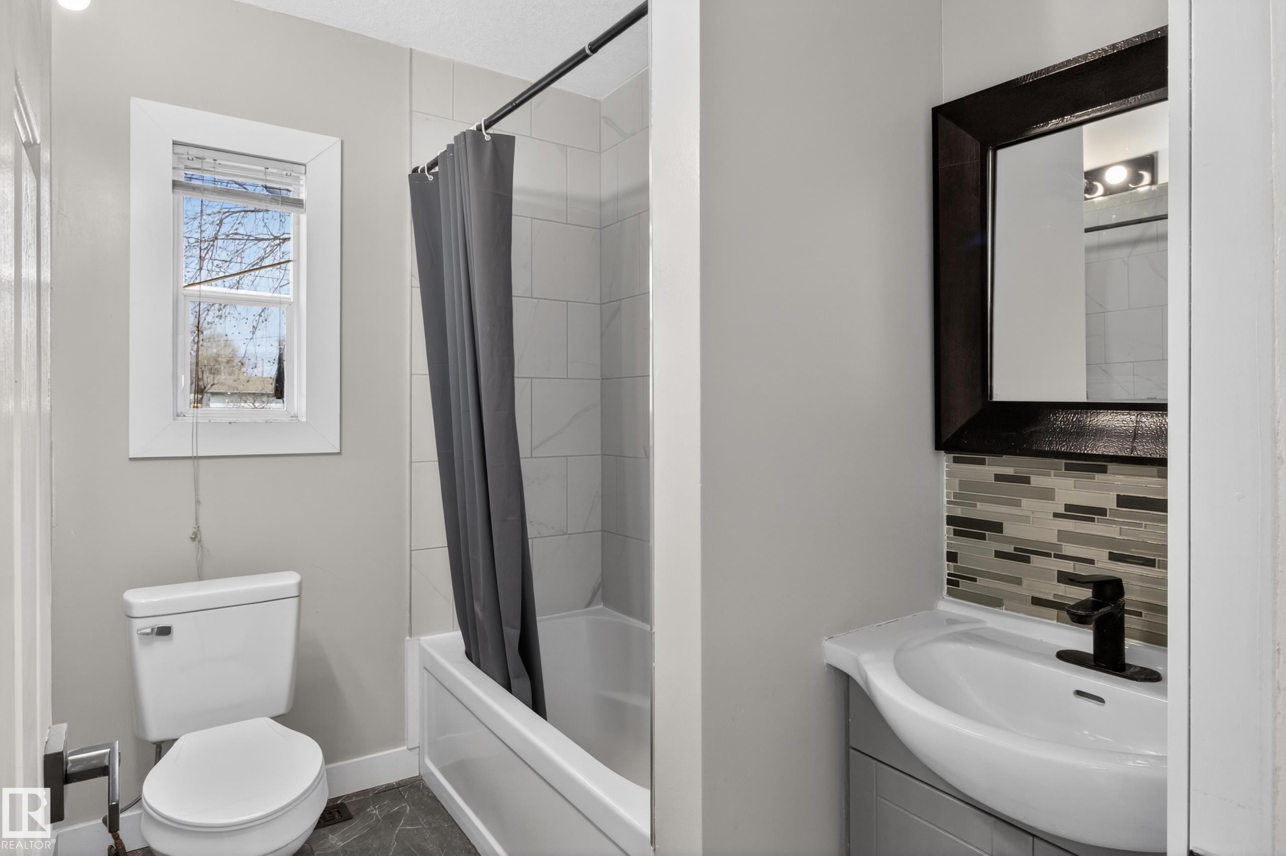 Bathroom featuring a white bathtub with tile surround, a toilet, and a vanity with an integrated sink - 8722 112 Avenue, Edmonton, AB - Indoor Photo Showing Bathroom