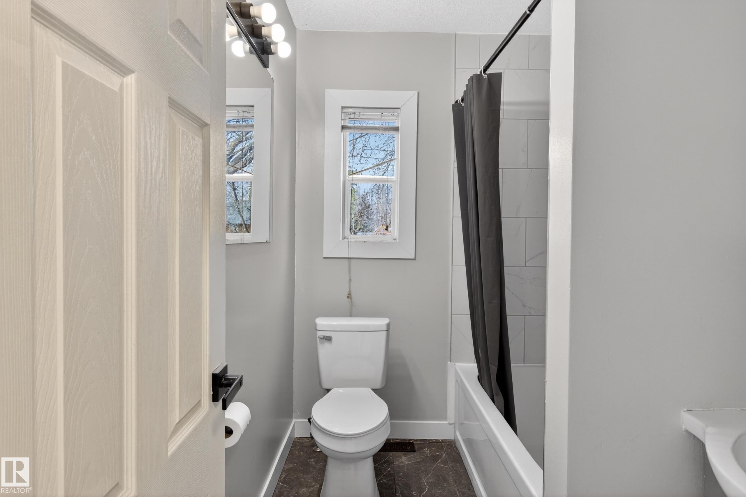 Bathroom featuring a white toilet, two windows, and a bathtub with white subway tile surround - 8722 112 Avenue, Edmonton, AB - Indoor Photo Showing Bathroom