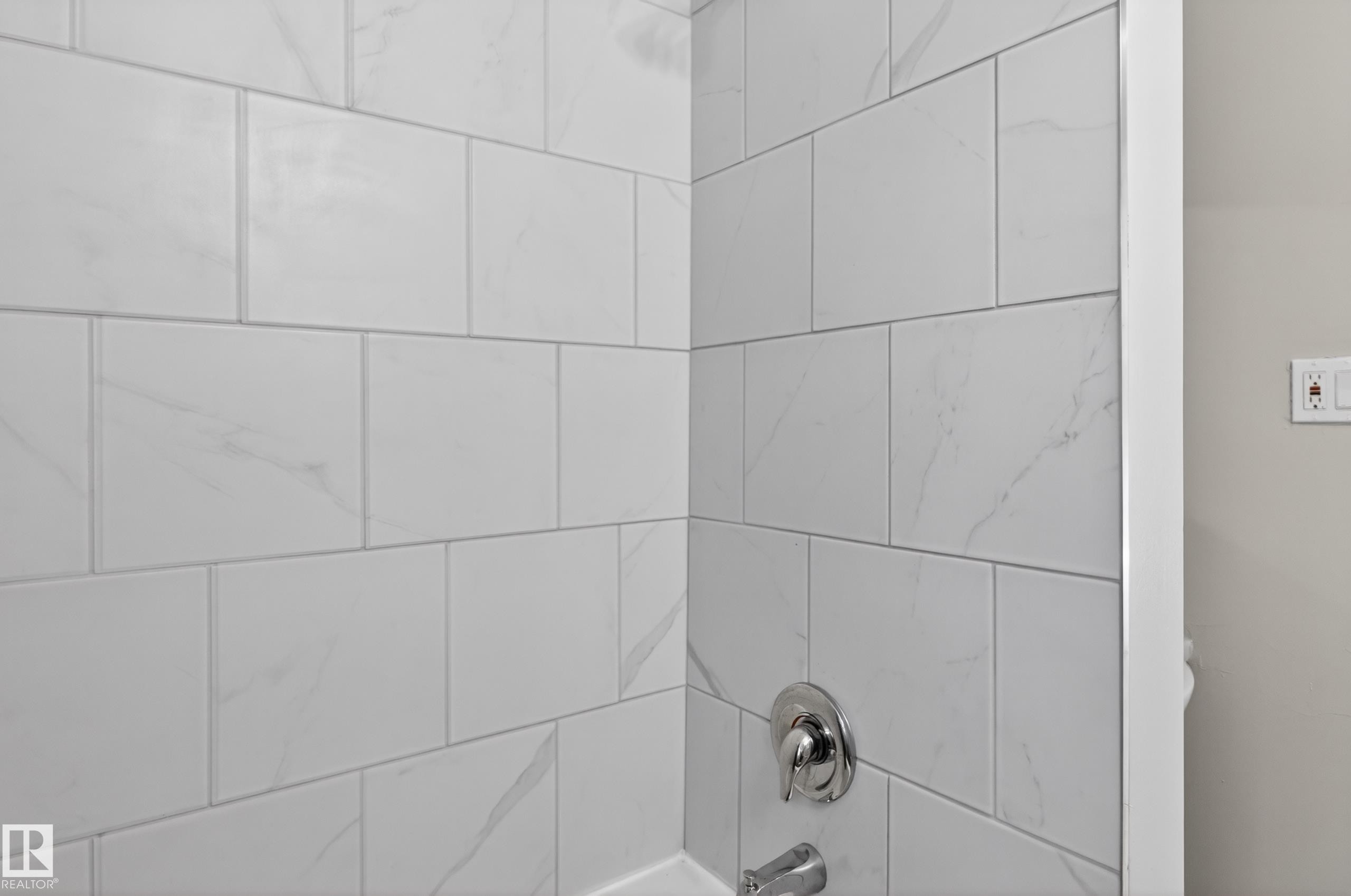 Shower enclosure with large format white tile, subtle veining, chrome fixtures, and a white tub surround - 8722 112 Avenue, Edmonton, AB - Indoor