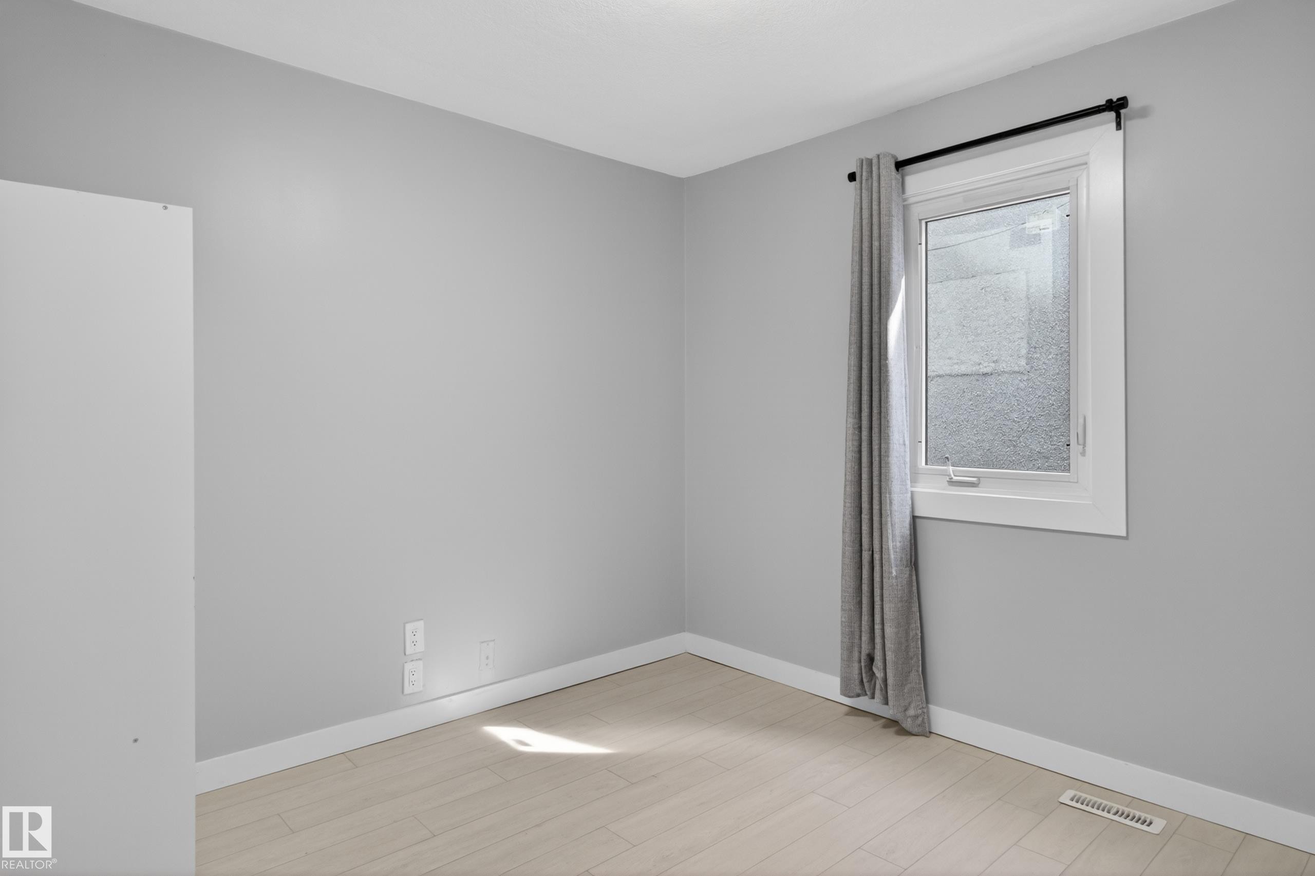 Room featuring light gray painted walls, wood-finish flooring, white baseboards, and a white-framed window - 8722 112 Avenue, Edmonton, AB - Indoor Photo Showing Other Room