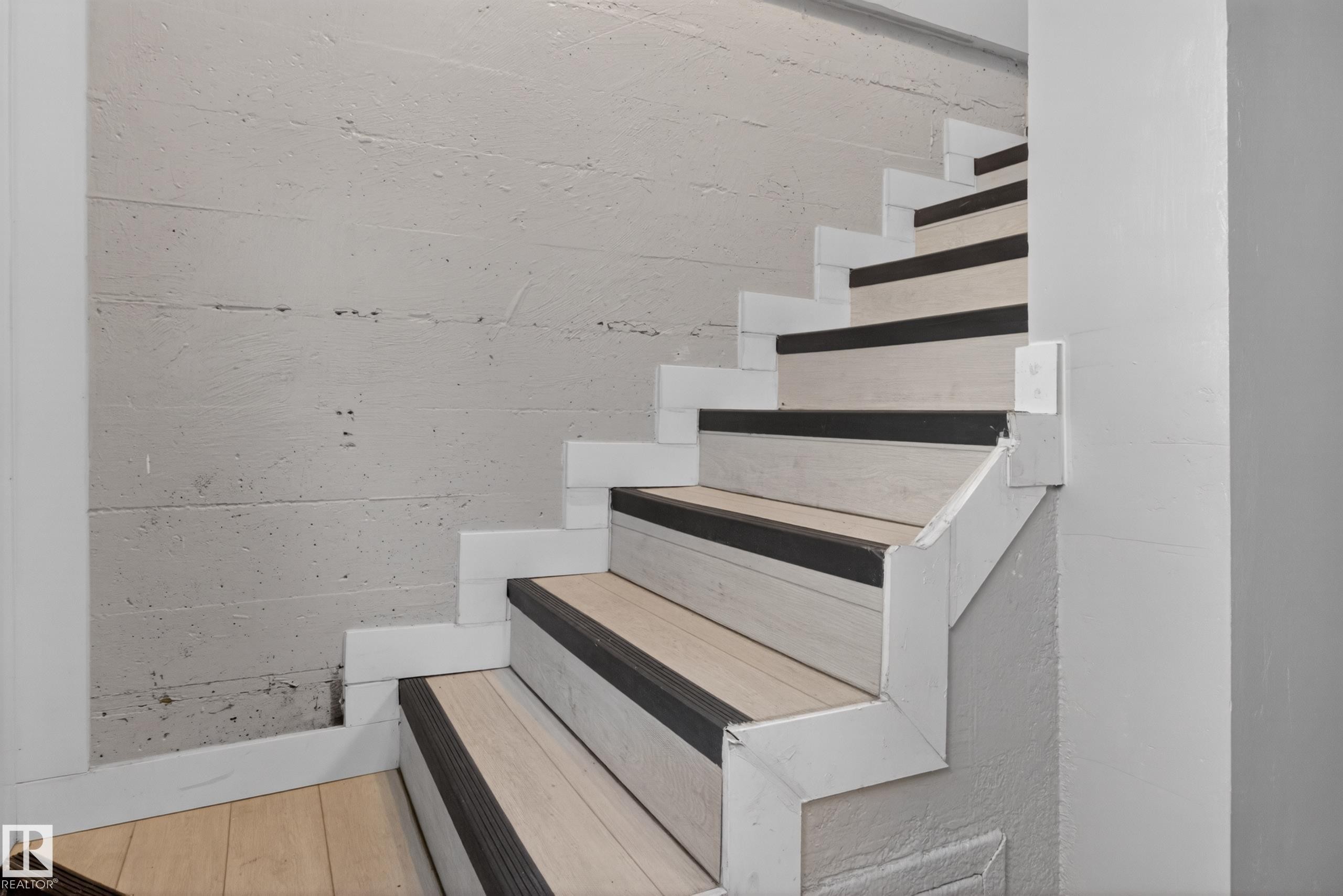 Staircase featuring wood-finish treads with dark anti-slip strips, white risers, and a textured concrete wall - 8722 112 Avenue, Edmonton, AB - Indoor Photo Showing Other Room