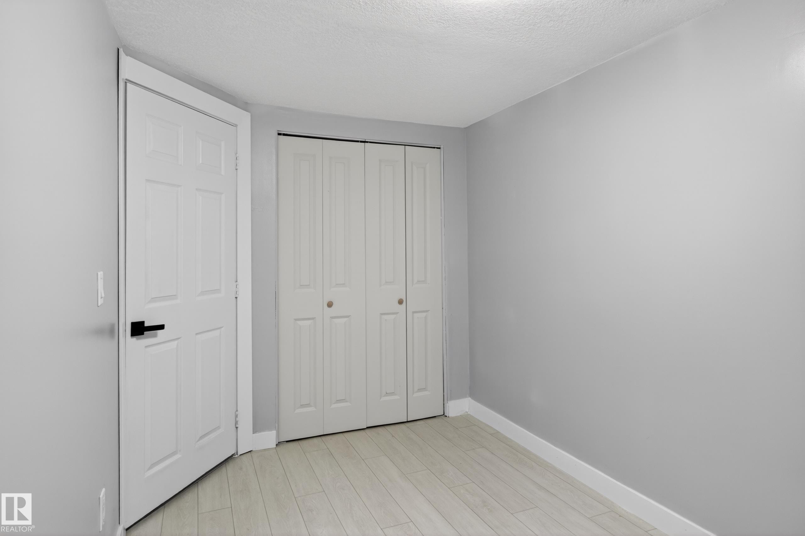 Interior room featuring light gray wall paint, white wood-finish flooring, and a white six-panel door with matte black hardware - 8722 112 Avenue, Edmonton, AB - Indoor Photo Showing Other Room