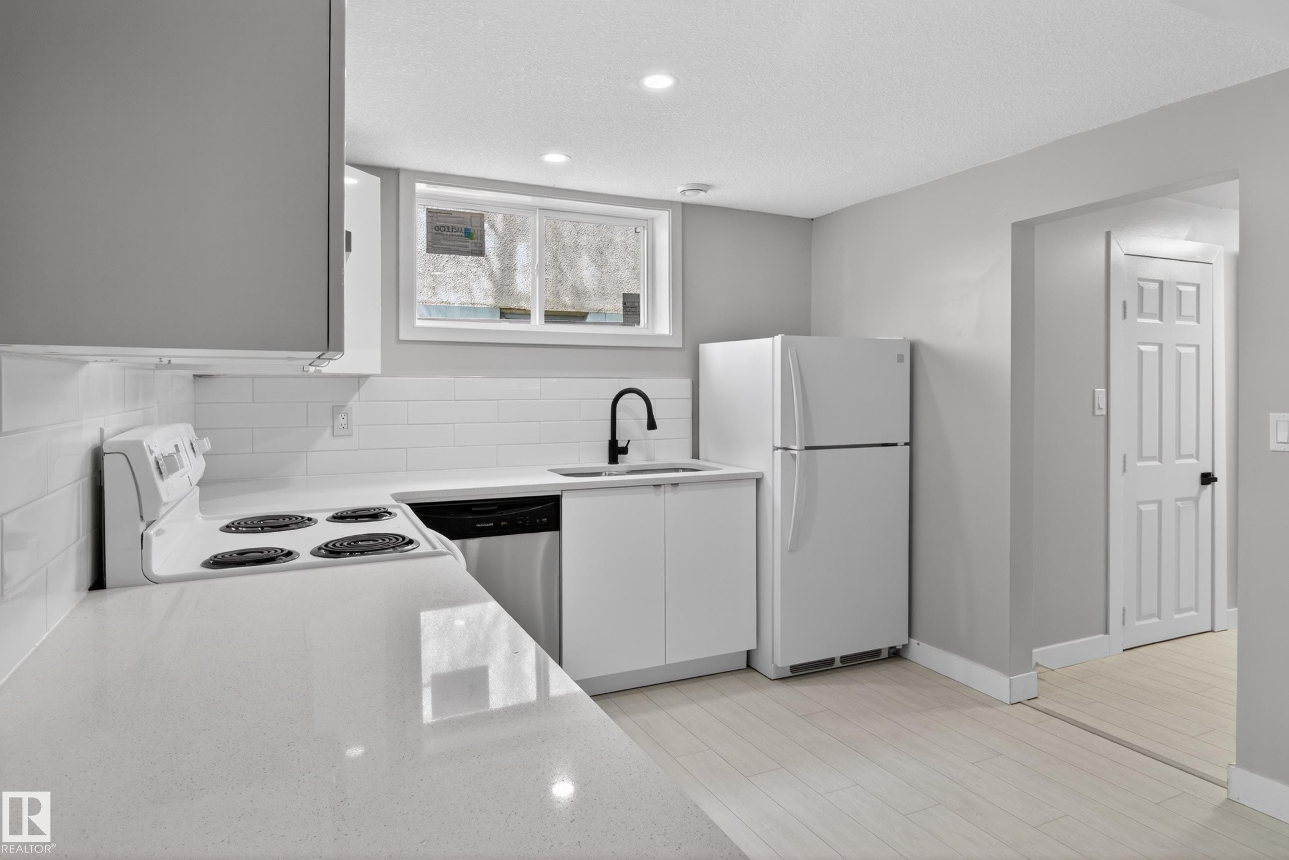 Modern kitchen featuring white cabinetry, light-toned countertops, a full suite of appliances, subway tile backsplash, and recessed lighting - 8722 112 Avenue, Edmonton, AB - Indoor Photo Showing Kitchen