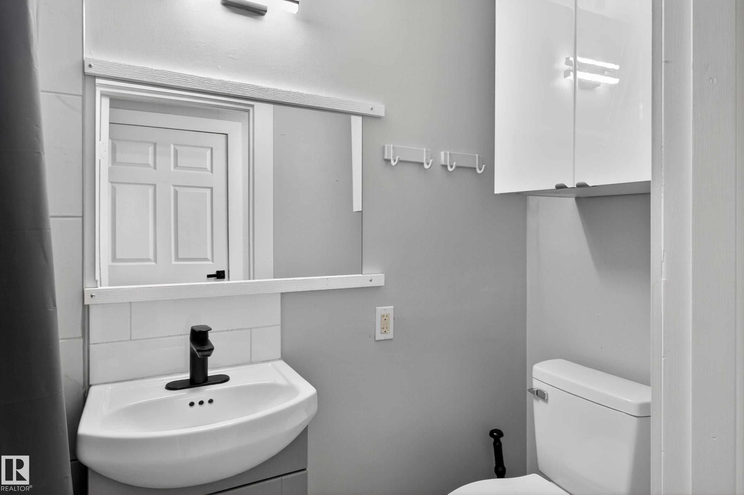 Modern bathroom featuring a corner-mounted sink with matte black faucet, subway tile backsplash, and wall-mounted storage cabinet - 8722 112 Avenue, Edmonton, AB - Indoor Photo Showing Bathroom