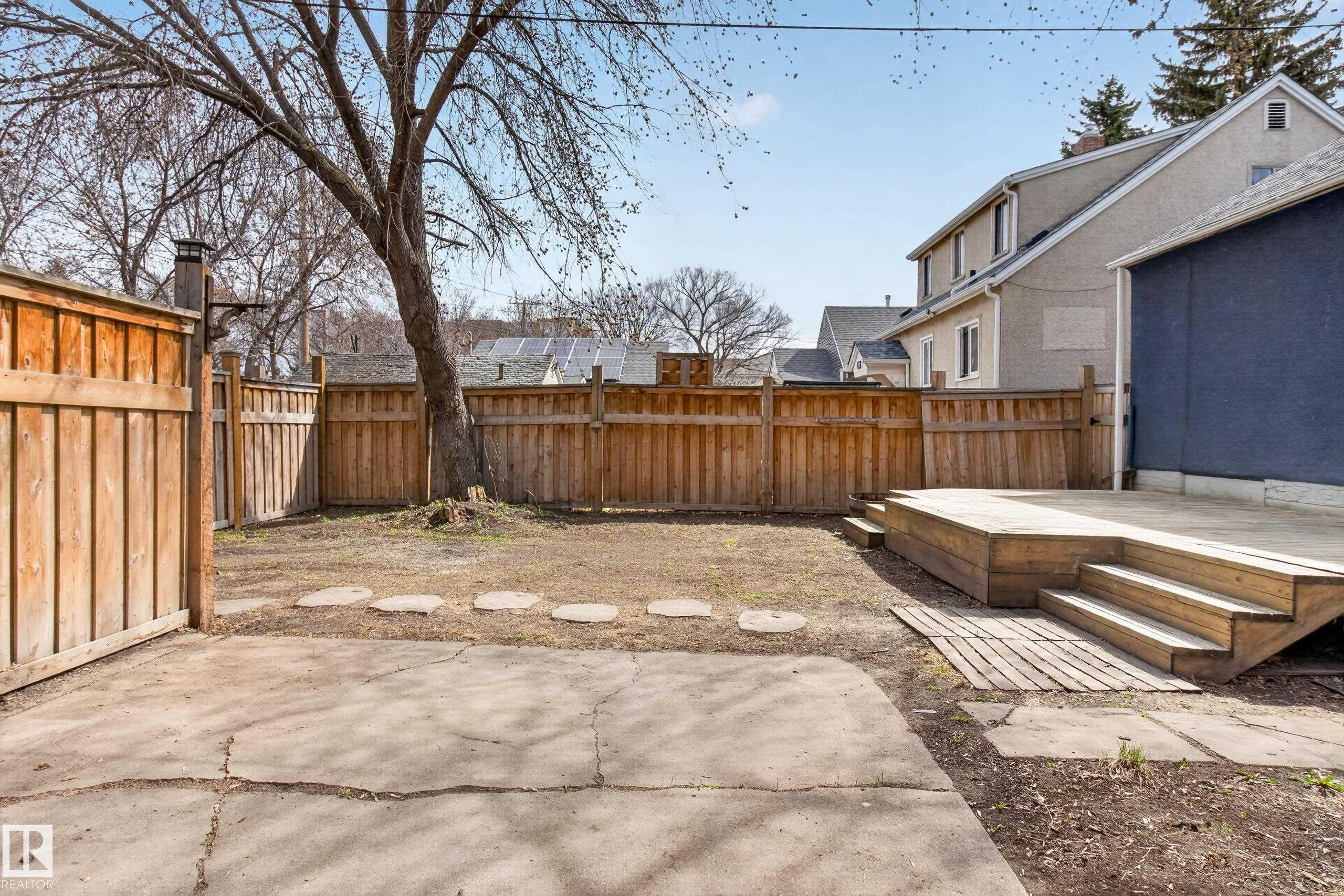 Expansive backyard featuring a large wooden deck with multiple steps, a full perimeter privacy fence, a concrete patio area, and mature trees - 8722 112 Avenue, Edmonton, AB - Outdoor