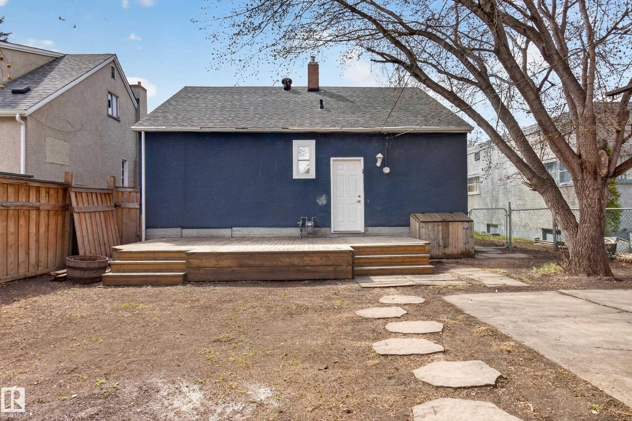Rear exterior featuring a spacious wooden deck with steps, a white entry door, and a single window - 8722 112 Avenue, Edmonton, AB - Outdoor