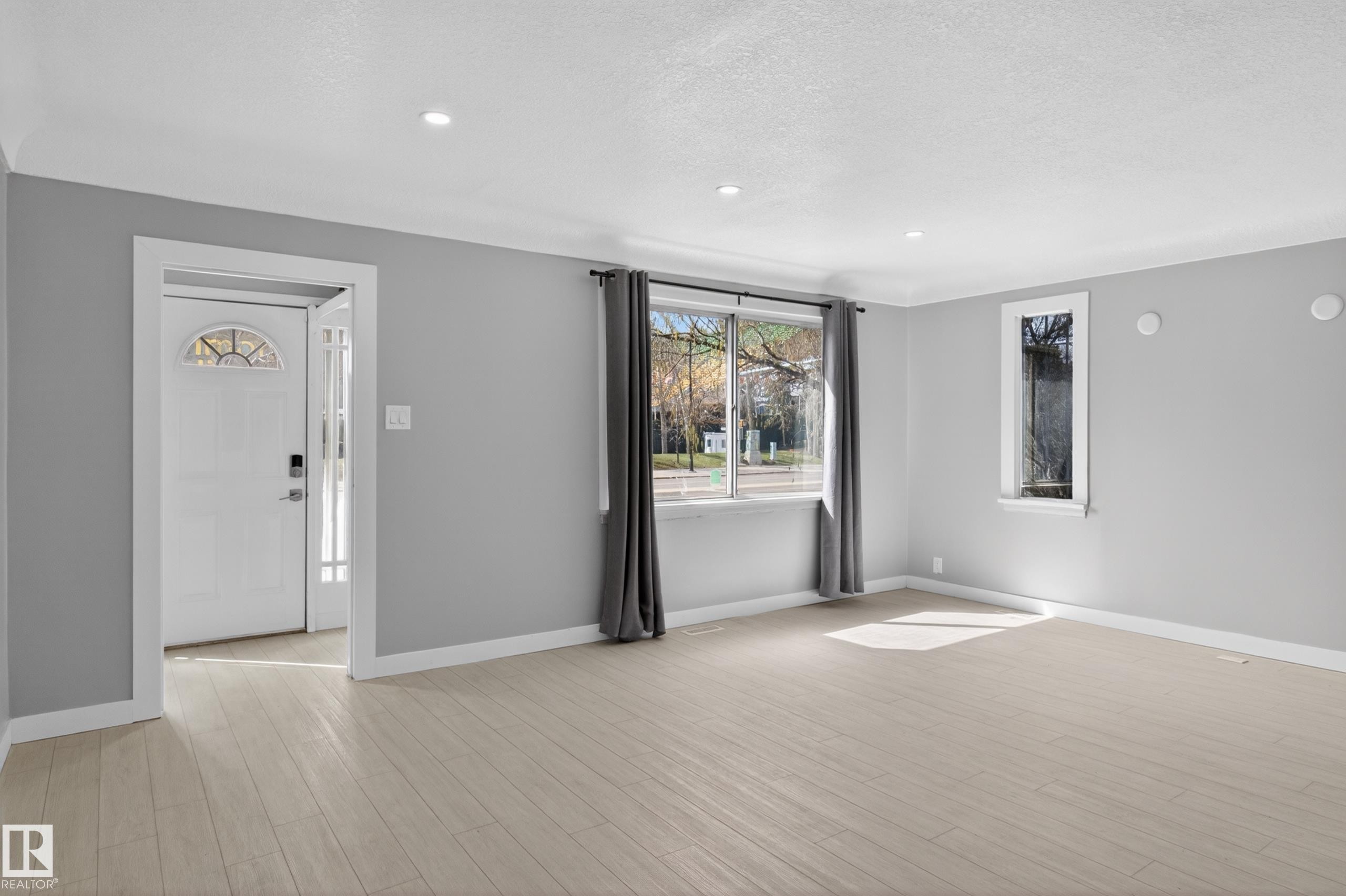 Spacious room featuring light wood-finish flooring, recessed lighting, and a white entry door with a decorative transom - 8722 112 Avenue, Edmonton, AB - Indoor Photo Showing Other Room