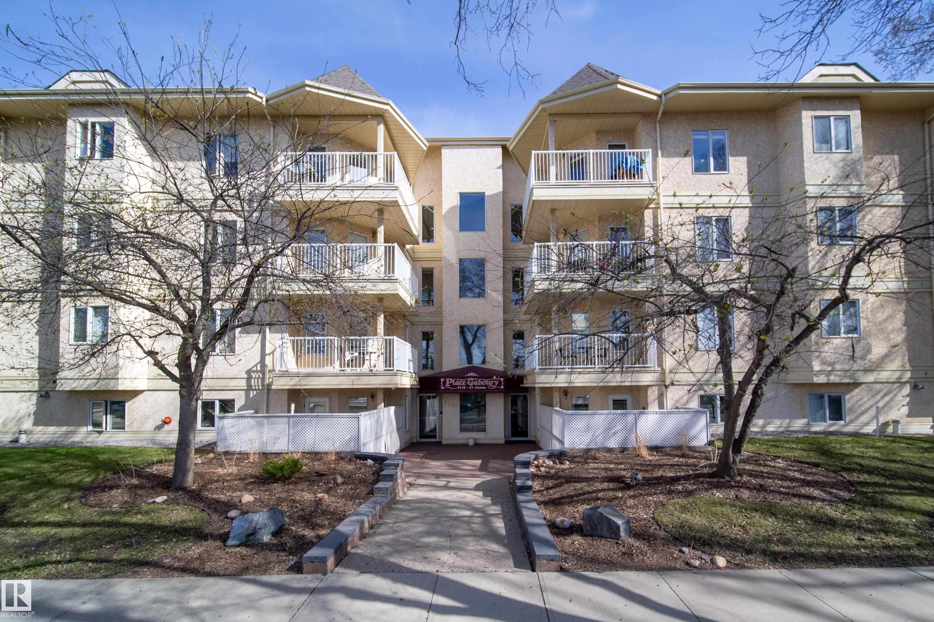 Multi-story residential building featuring a stucco facade, multiple balconies with white railings, and a central entryway - 302 9138 83 Avenue, Edmonton, AB - Outdoor With Balcony With Facade